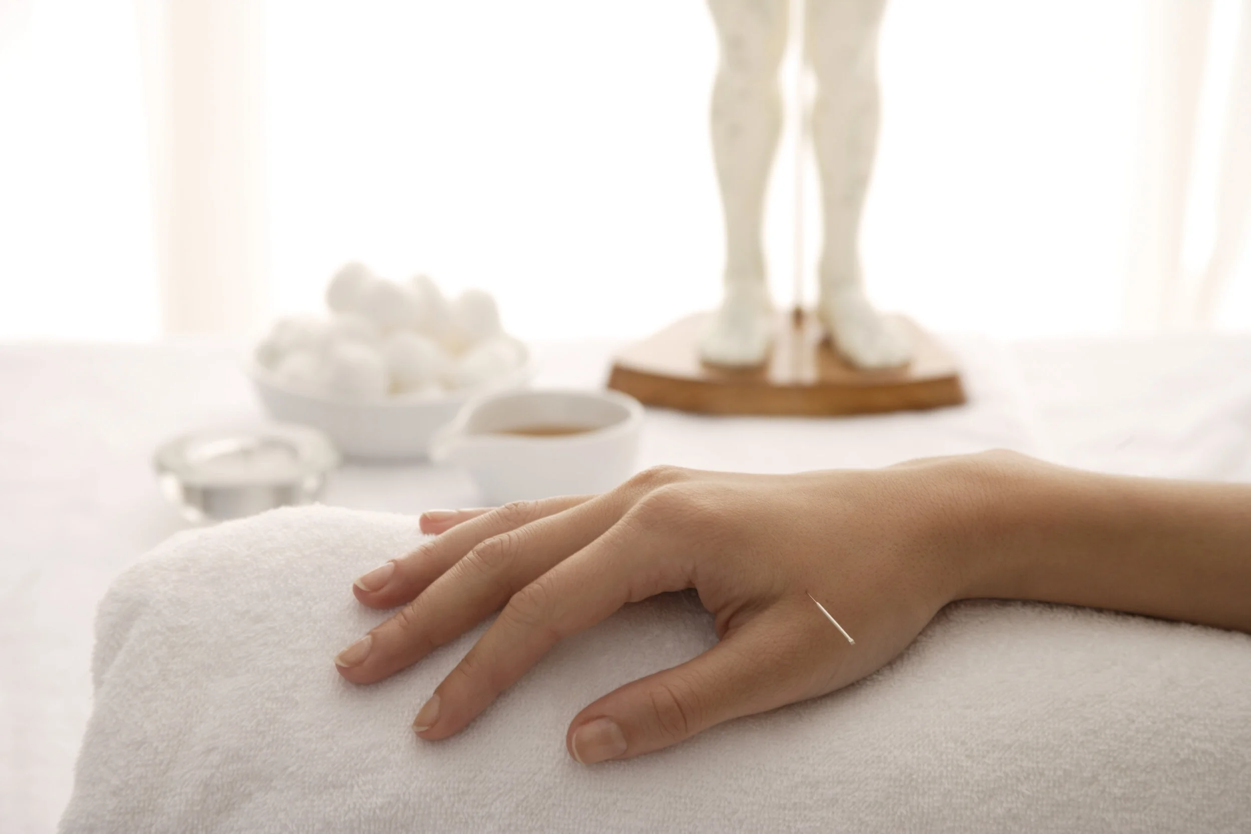 Hand resting on a white towel in a spa or massage setting, with massage tools and a statue in the background