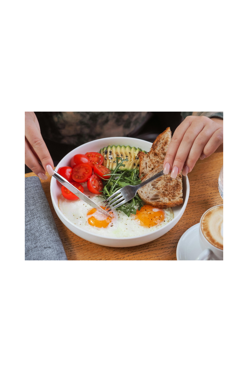 Hands shown holding fork and knife and eating eggs, tomatoes, wheat bread and avocado