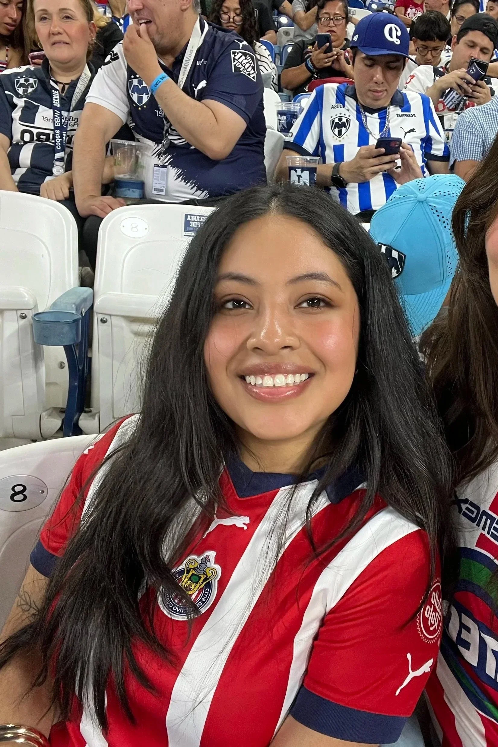 Woman standing outdoors near desert plants, wearing a sleeveless top, jeans, and tan shoes, with sunlight casting shadows.