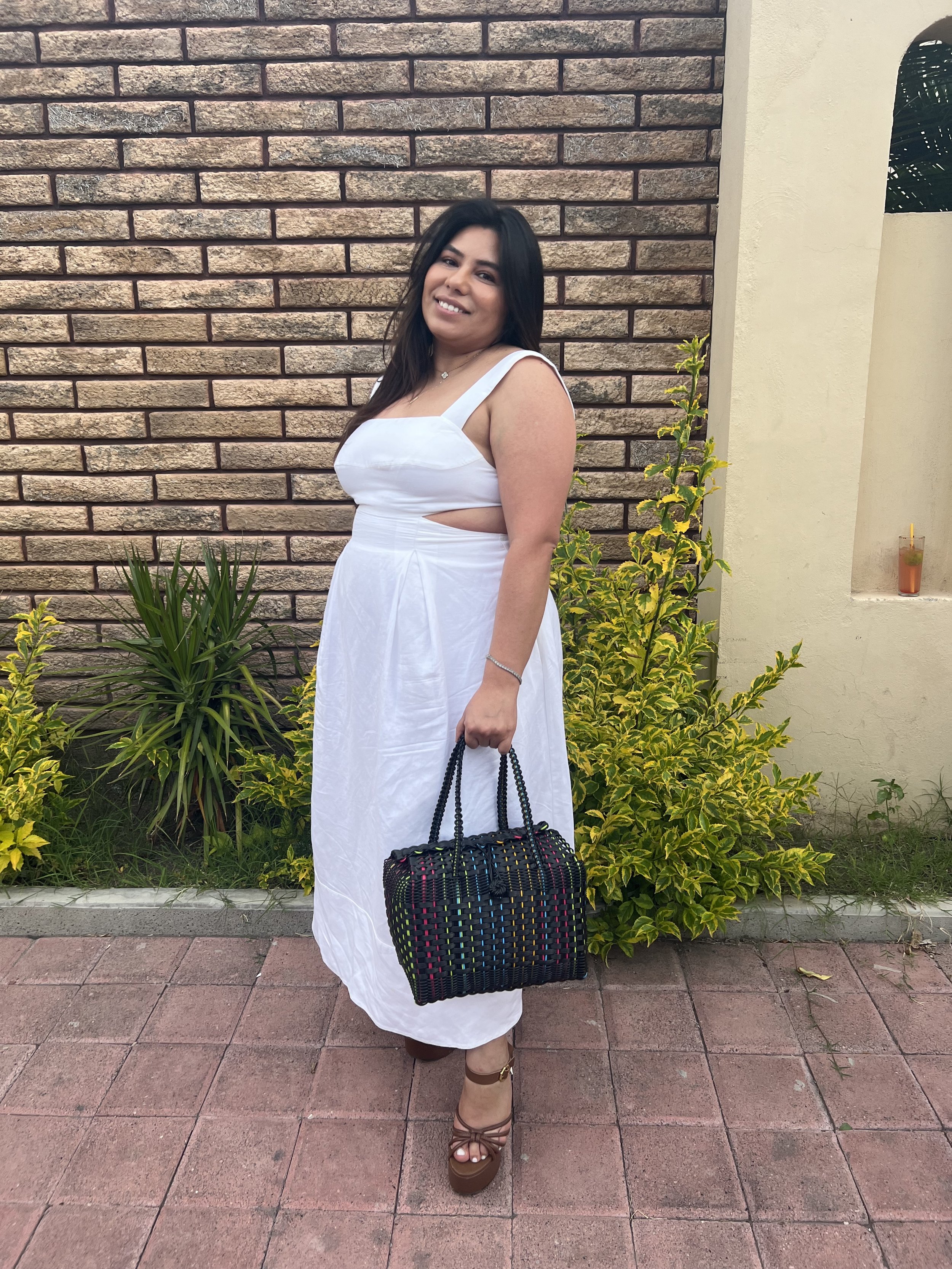 Two women sitting in the backseat of a car. The woman on the left has long dark hair and is smiling at the camera. The woman on the right has long brown hair, is wearing large black sunglasses, and is looking at the camera with a slight smile.