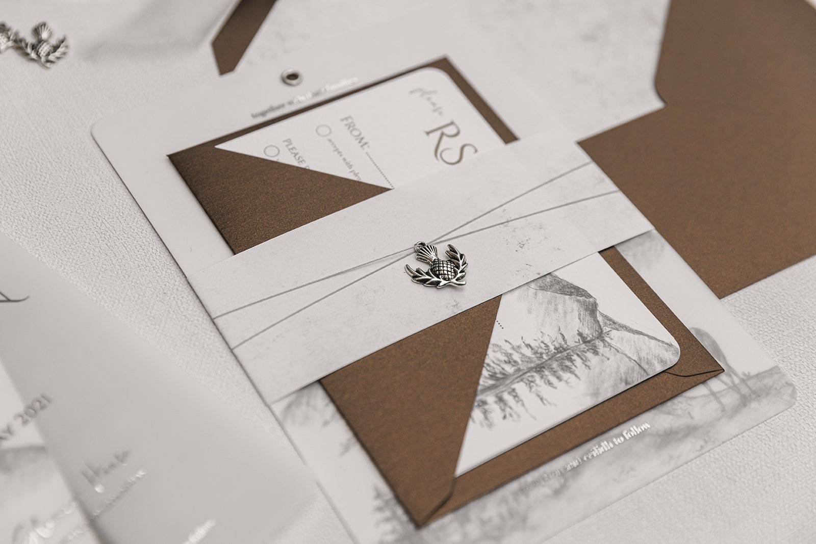 Silver-foiled Highland Romance Charmed Invite™ with silver thistle charm, and 'Highland Bronze Shimmer' envelopes