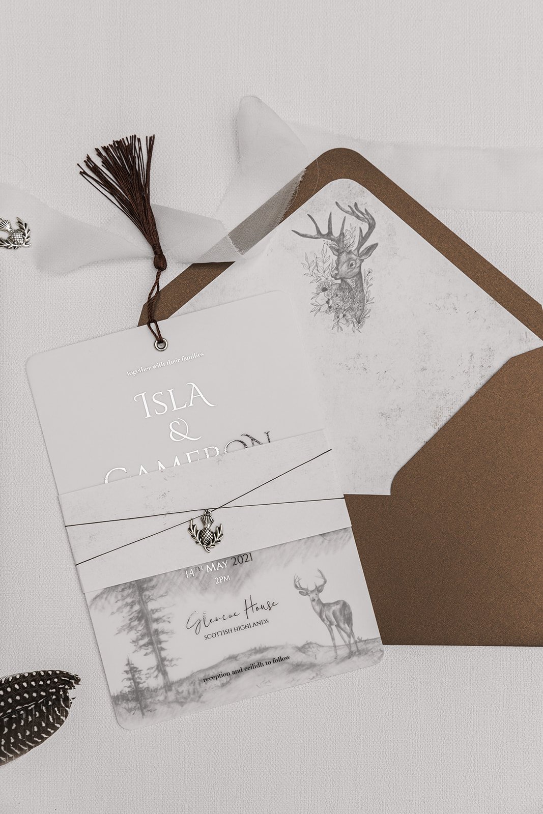 Silver-foiled Highland Romance Charmed Invite™ with silver thistle charm, bronze tassel, and lined 'Highland Bronze Shimmer' envelope