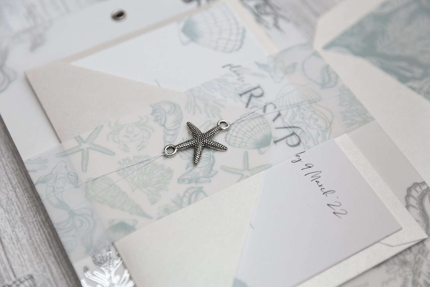 Beachcomber Sea Spray Charmed Invite™ with silver starfish charm, sea illustrations vellum belly wrap, and 'Pearl Oyster' RSVP envelope