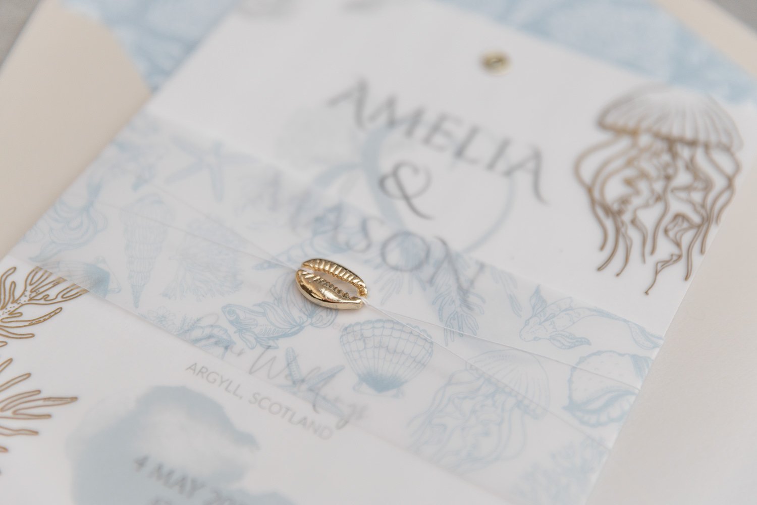 Gold-foiled Charmed Invite™, will gold sea illustrations overlay, illustrated vellum belly band and gold cowrie shell charm