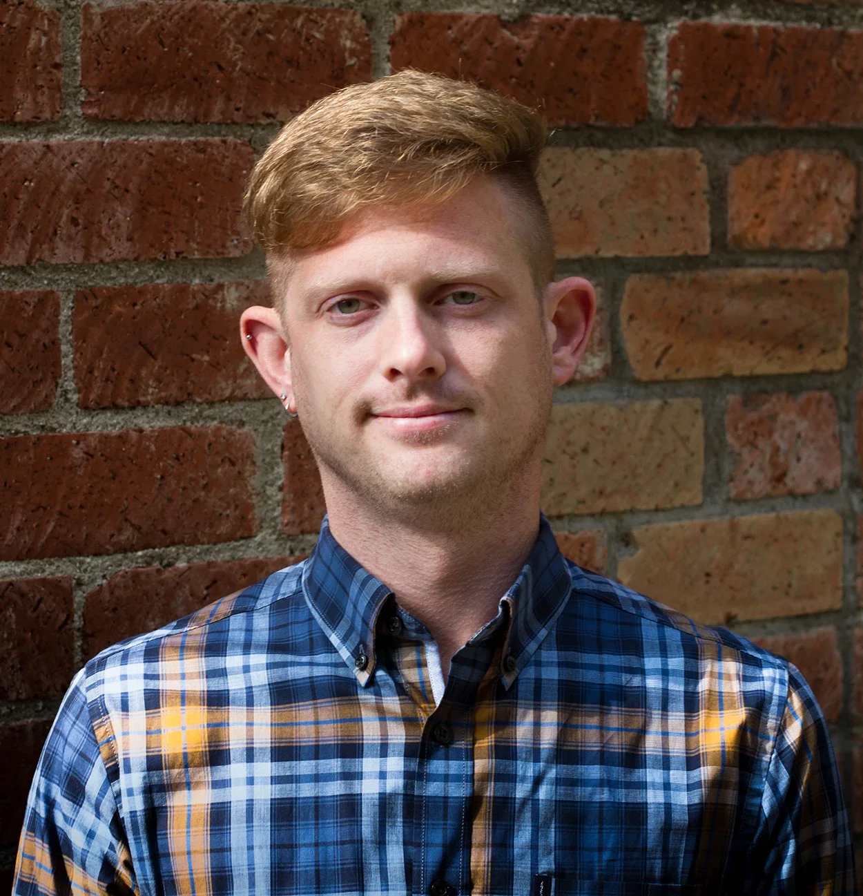 headshot of daryl short blonde hair, wearing a blue checked collared shirt