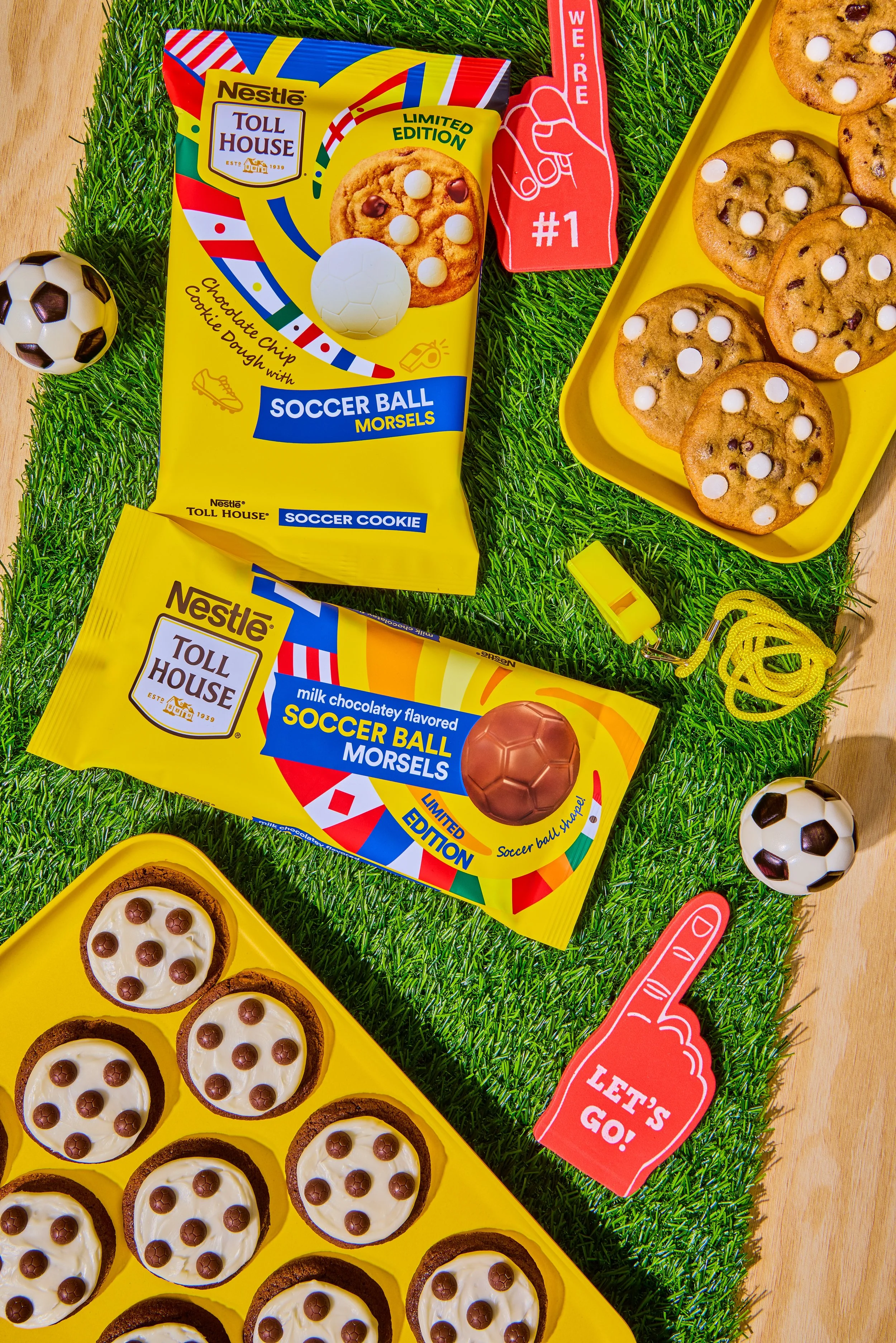 Packaging of Nestlé Toll House soccer ball cookies and molded chocolates, with plates of cookies and mini soccer balls on a playground-style grass surface, toy whistle, and foam finger with 'Let's Go!' on a wooden table.