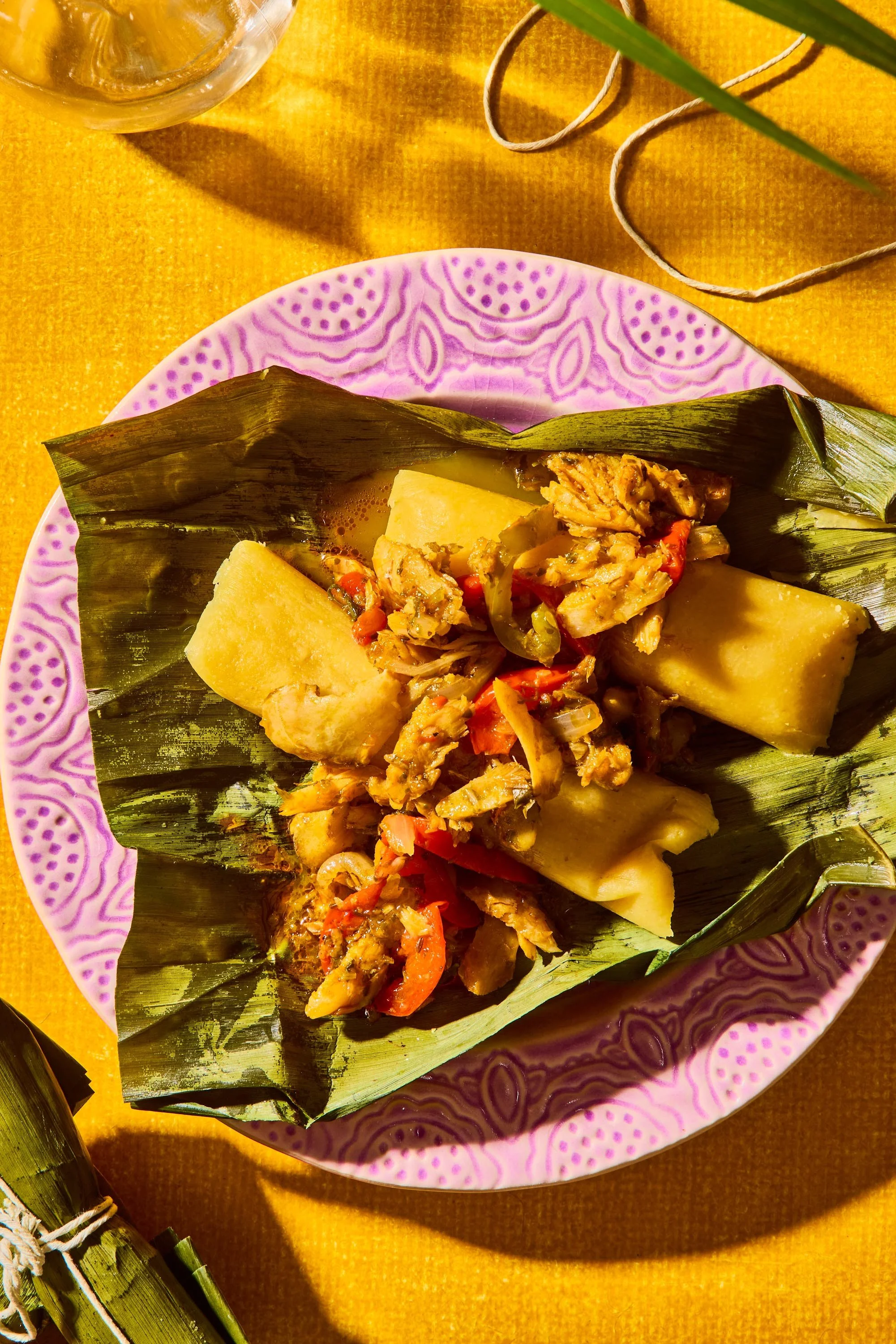 Traditional Central American dish served on a patterned pink and purple plate, placed on a yellow cloth, with banana leaf lining containing the dish.