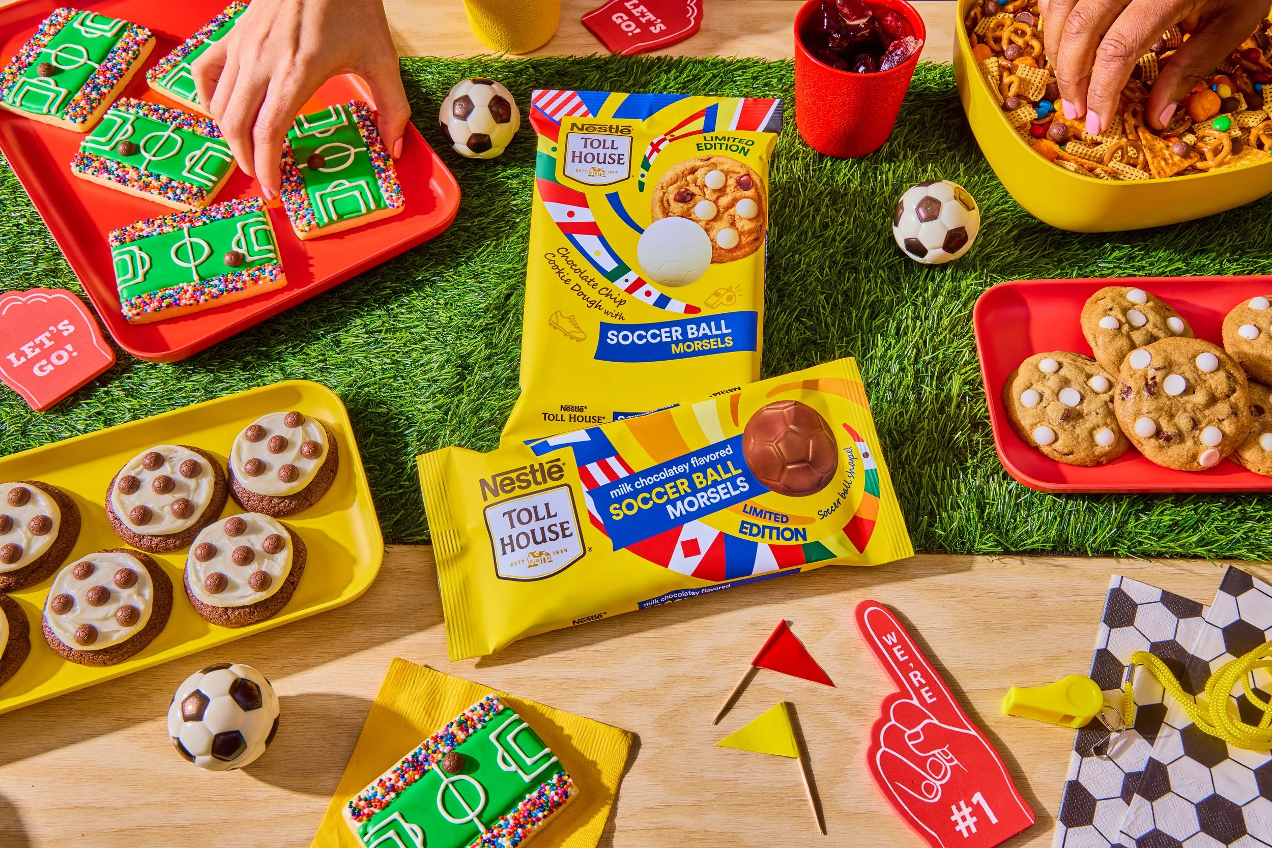 A table set with football-themed cookies, cupcakes, and snacks for a soccer game party, featuring soccer ball toys, small flags, and party items.