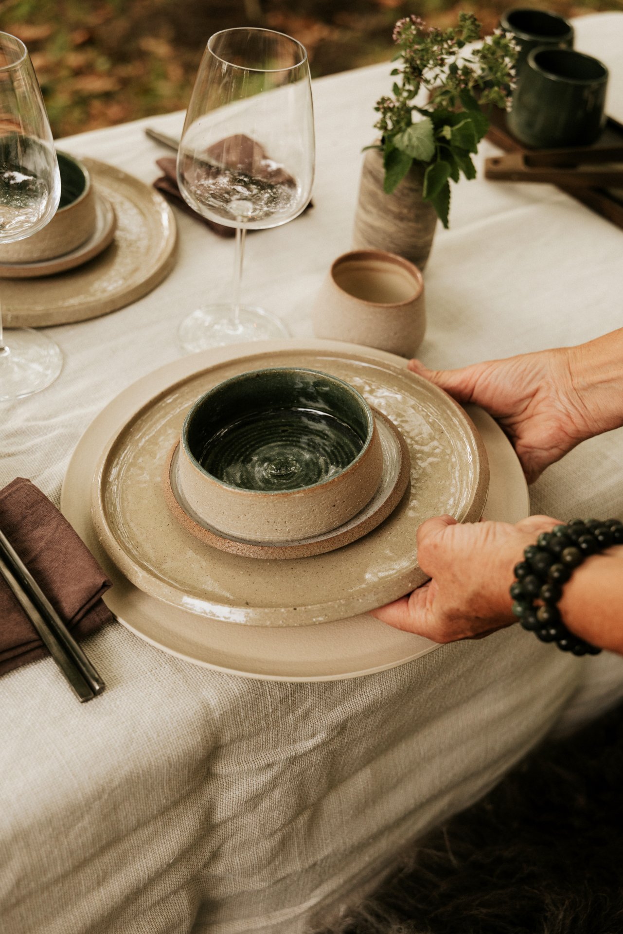Vrouwenhand die tafel dekt met keramische borden en kommen.