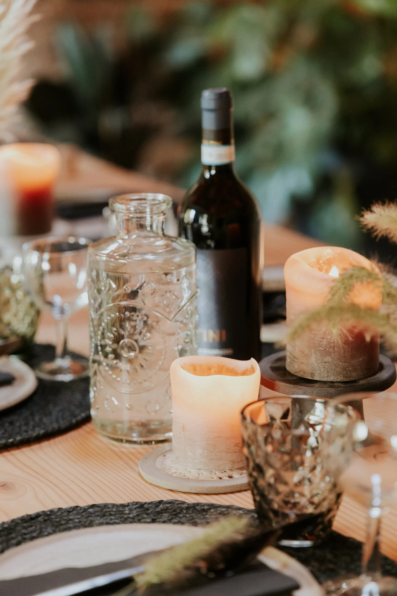 Een gedekte tafel met een fles wijn, glazen, kaarsen en decoraties in een gezellige setting.