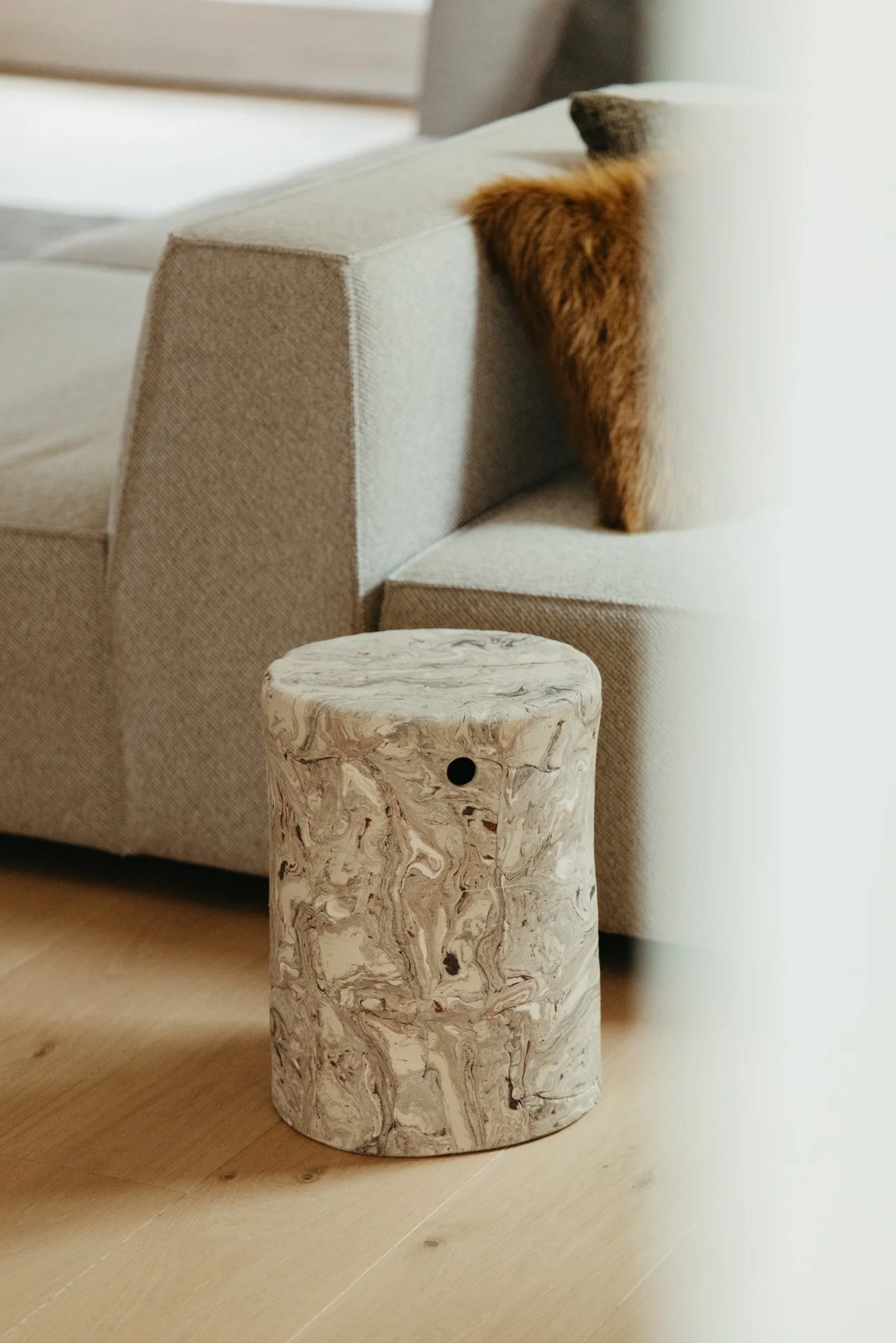 Een kruk van keramiek met een beige bank op de achtergrond en een houten vloer.