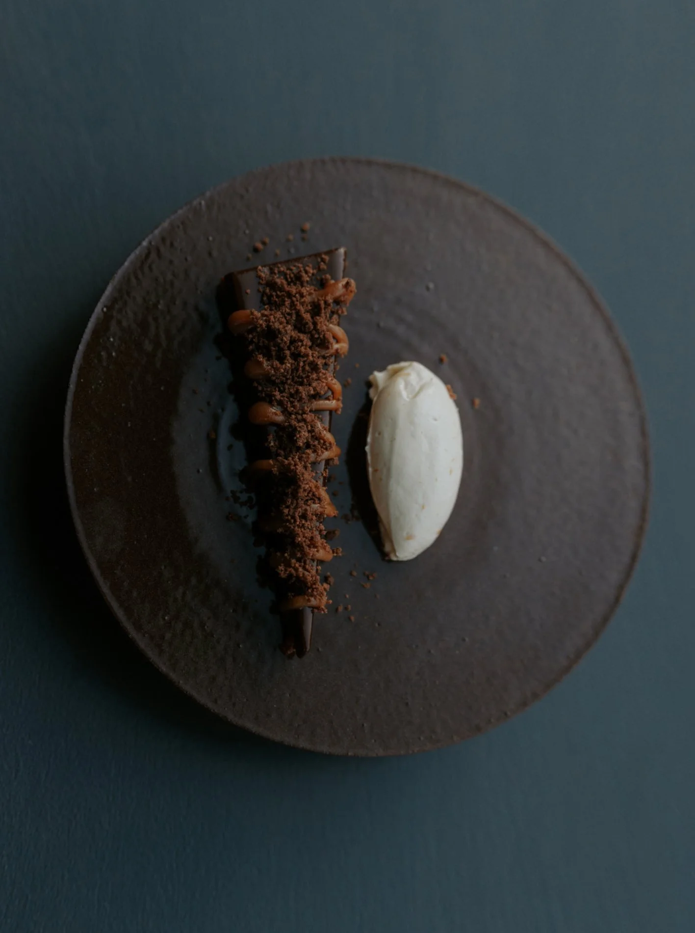 Zwart bord met wit dessert er op, blauwe achtergrond.  Atelier Pyotr Morf.