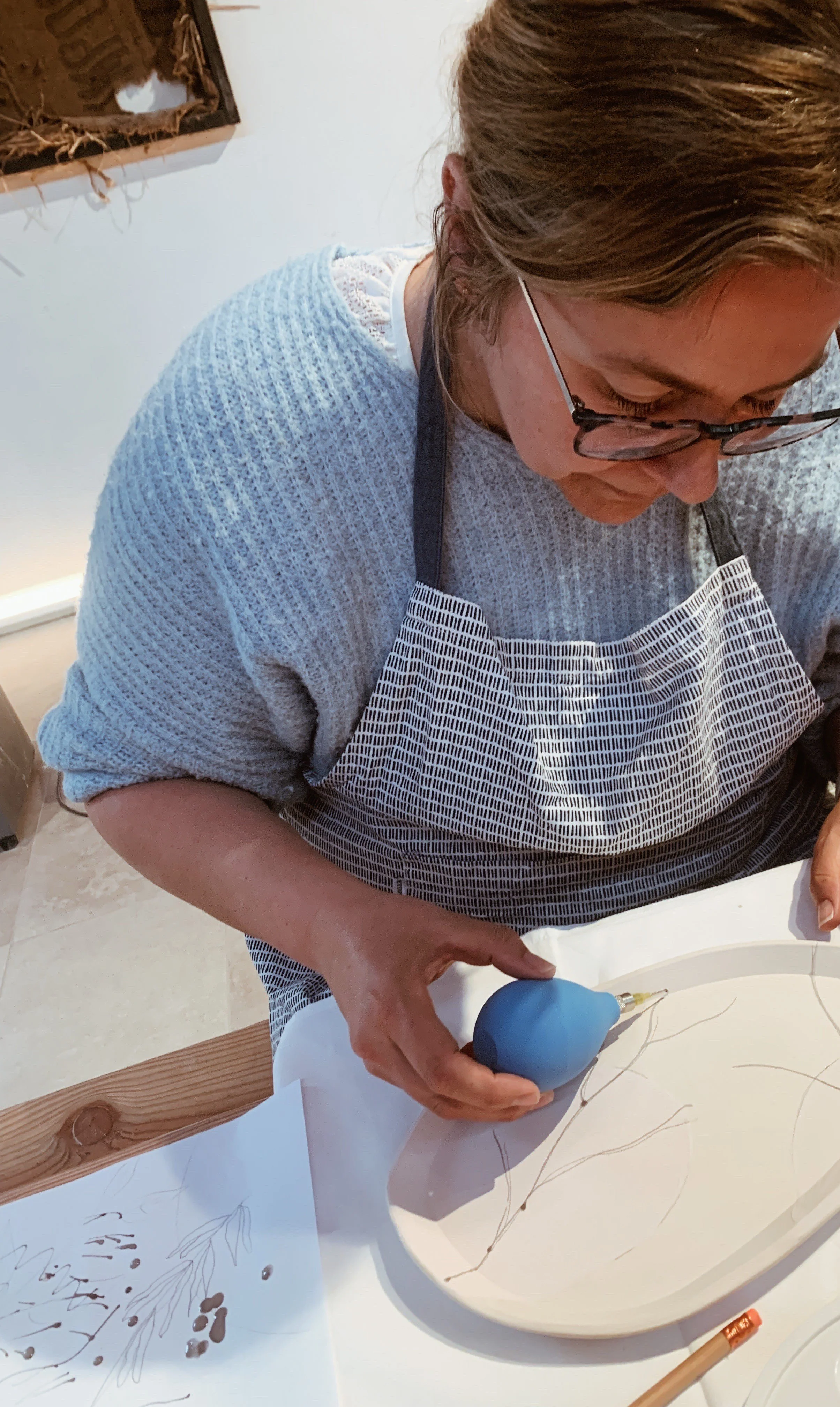 Mevrouw met blauwe tshirt die bezig is met pottery painting op een bord.