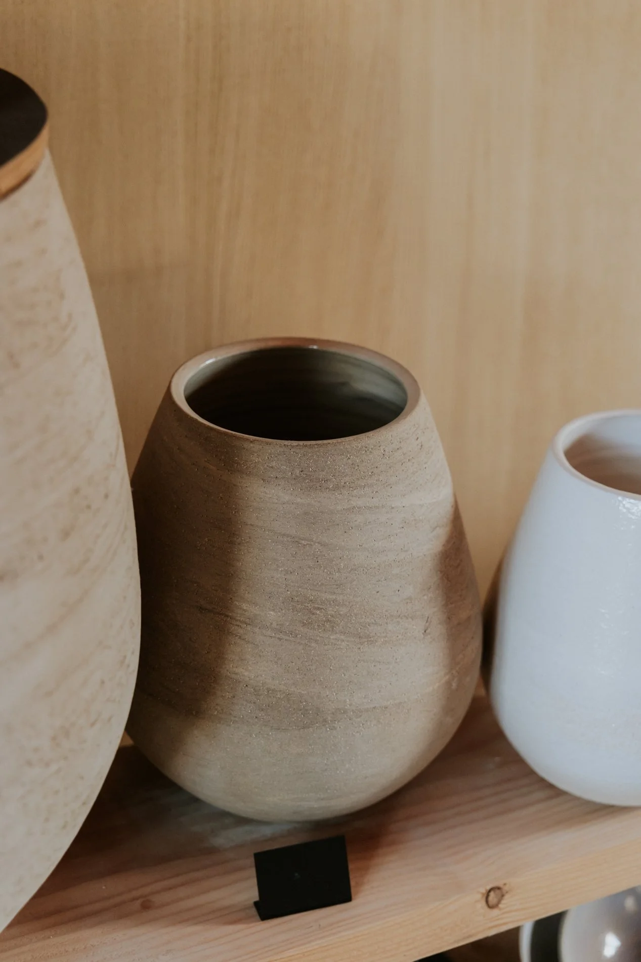 Drie keramische vazen in natuurlijke tinten op een houten plank.