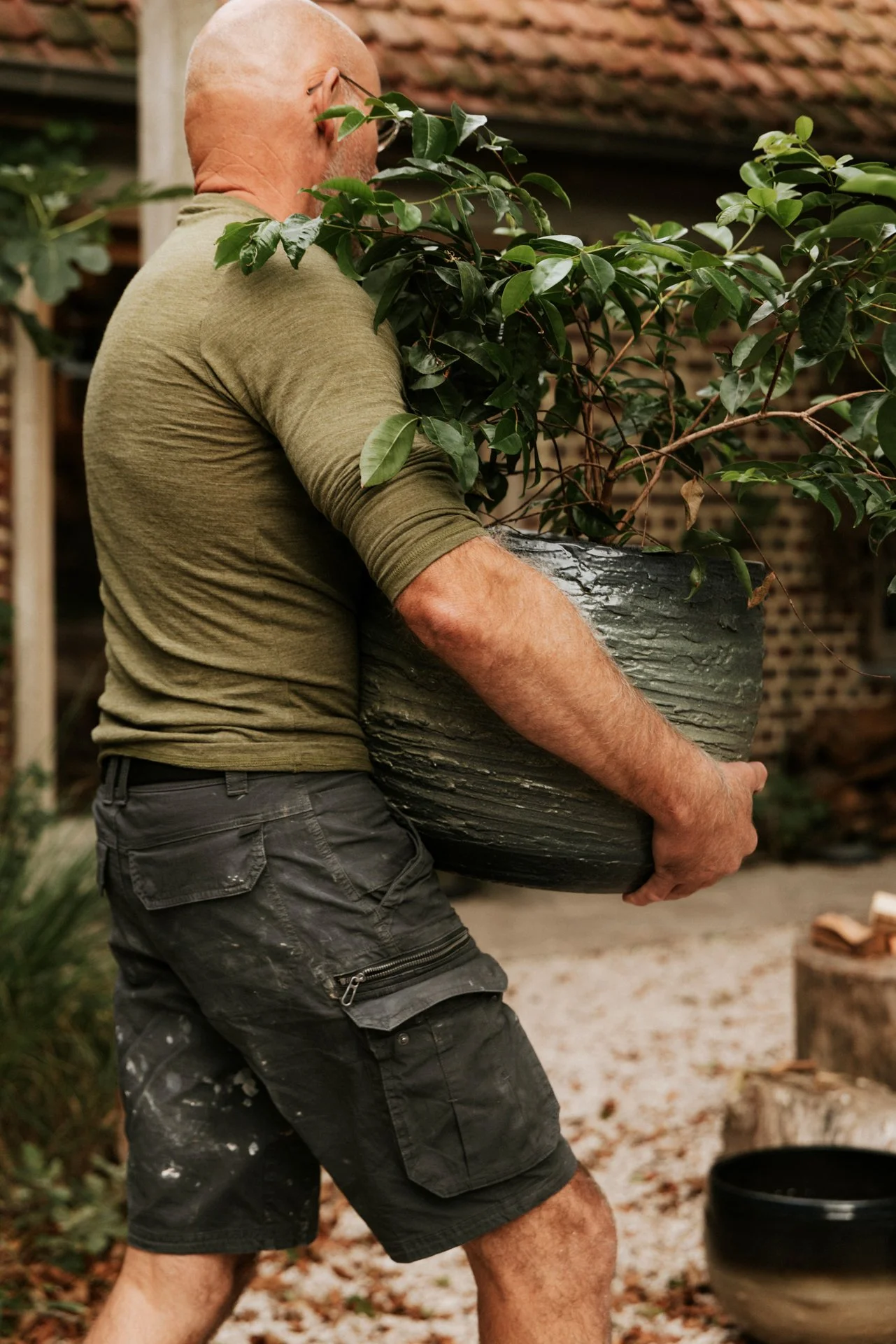 Man die een grote bloempot met een groene plant vasthoudt in een tuin of achtertuin.
