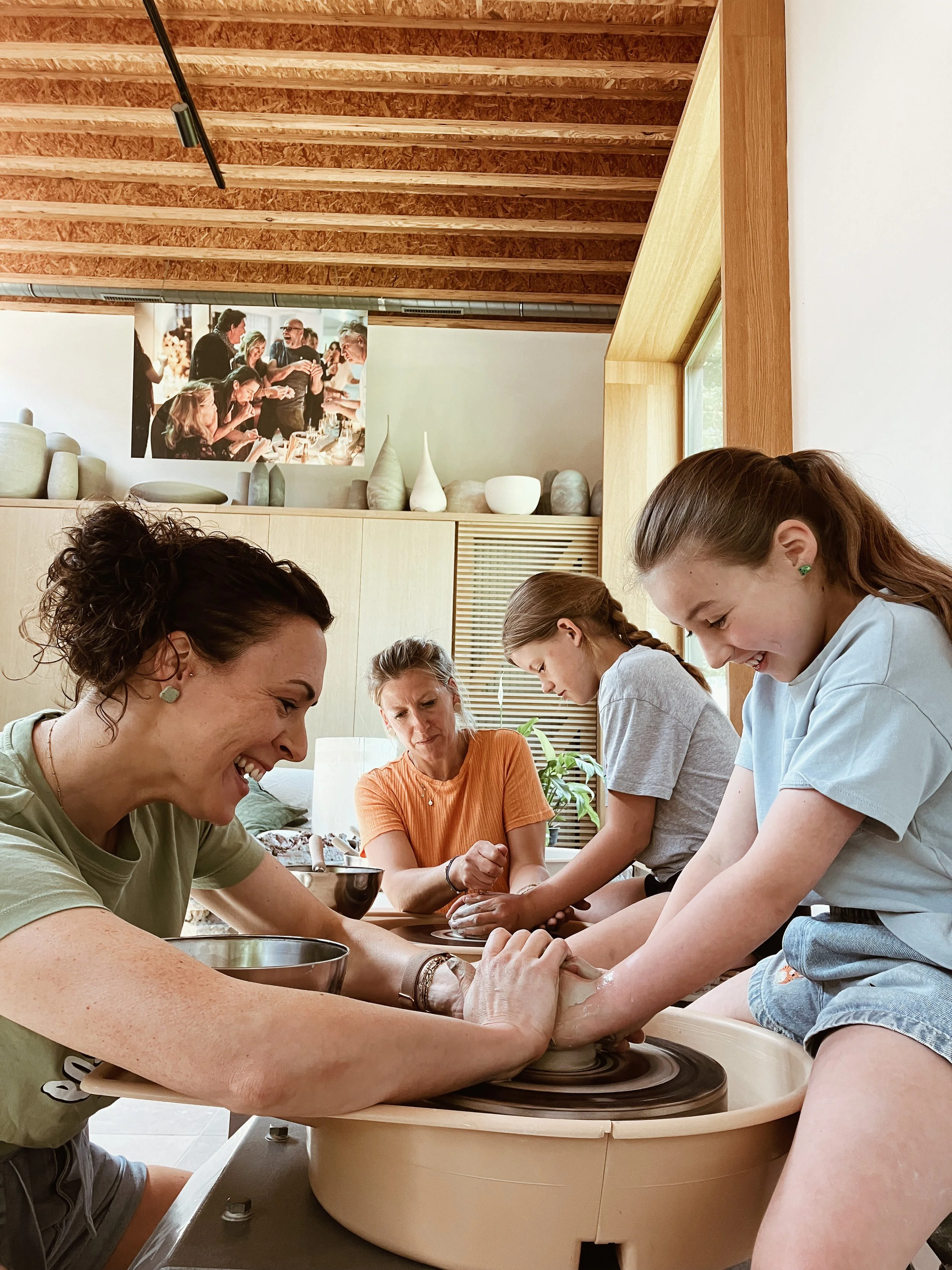 Moeders met hun dochter die een kopje aan het draaien zijn in klei in een atelier.