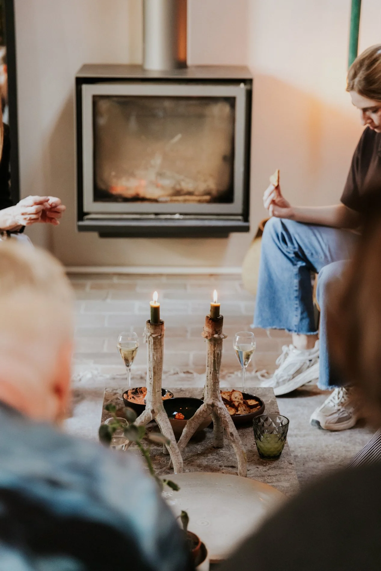Gezelschap mensen dat binnen een huis samen een gezellige bijeenkomst heeft, met een centraal gedekte tafel en een brandende kaars.