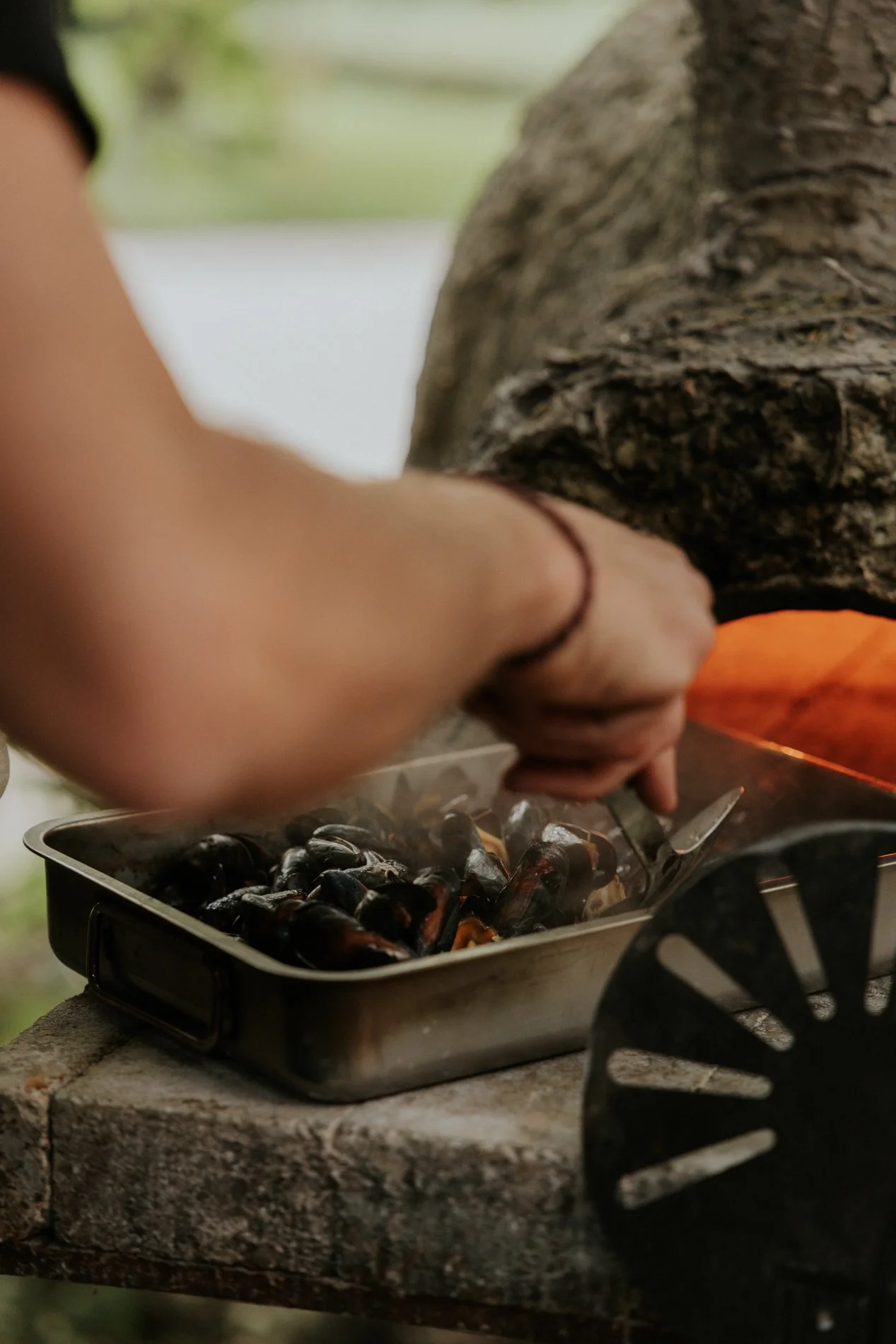 Mossels die afgebakken worden in de klei houtoven. Hand van een man.