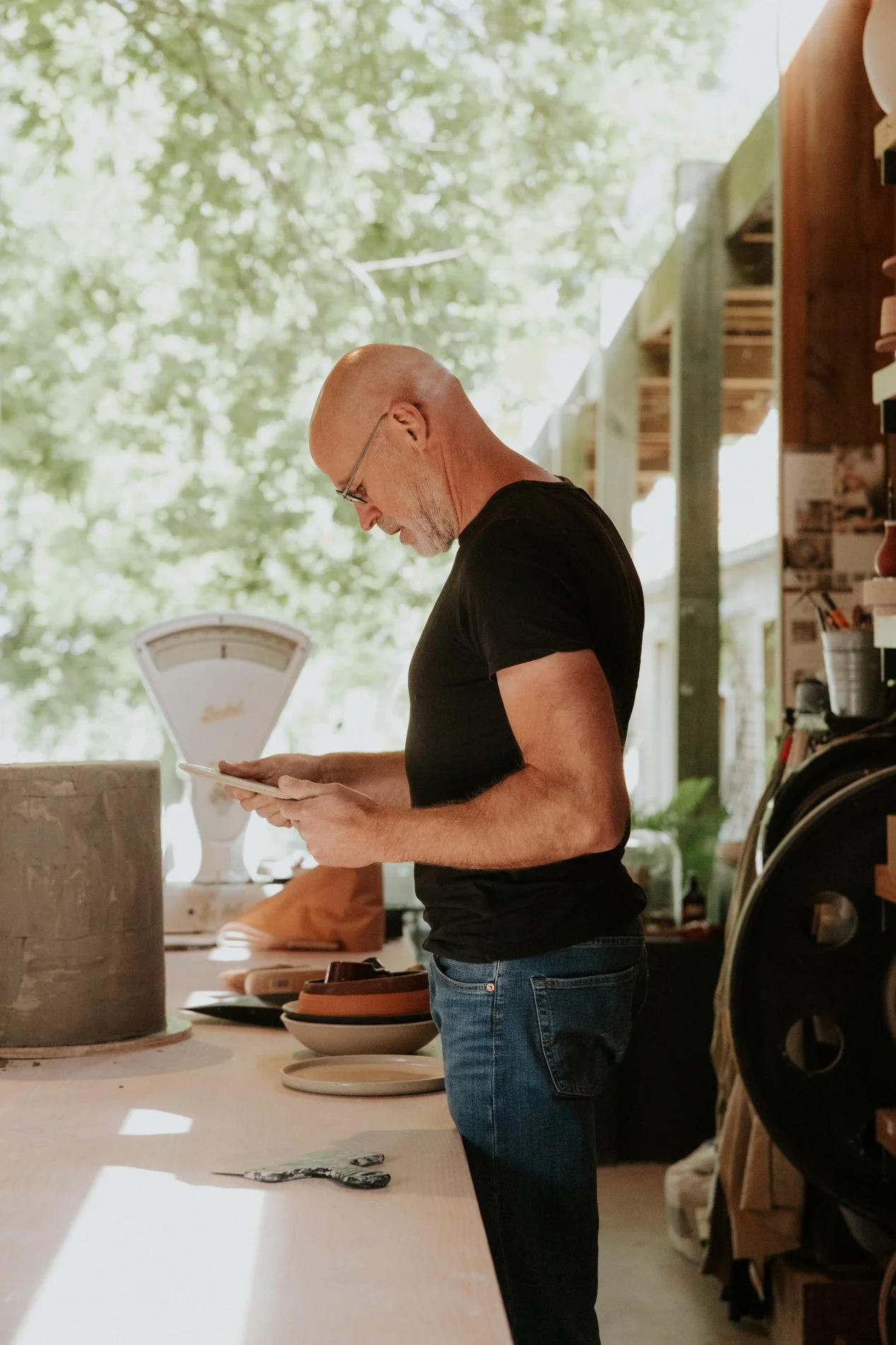 Pyotr Morf in zijn atelier die een bord inspecteerd. Op de achtergrond een weegschaal en de tuin.  Atelier Pyotr Morf.