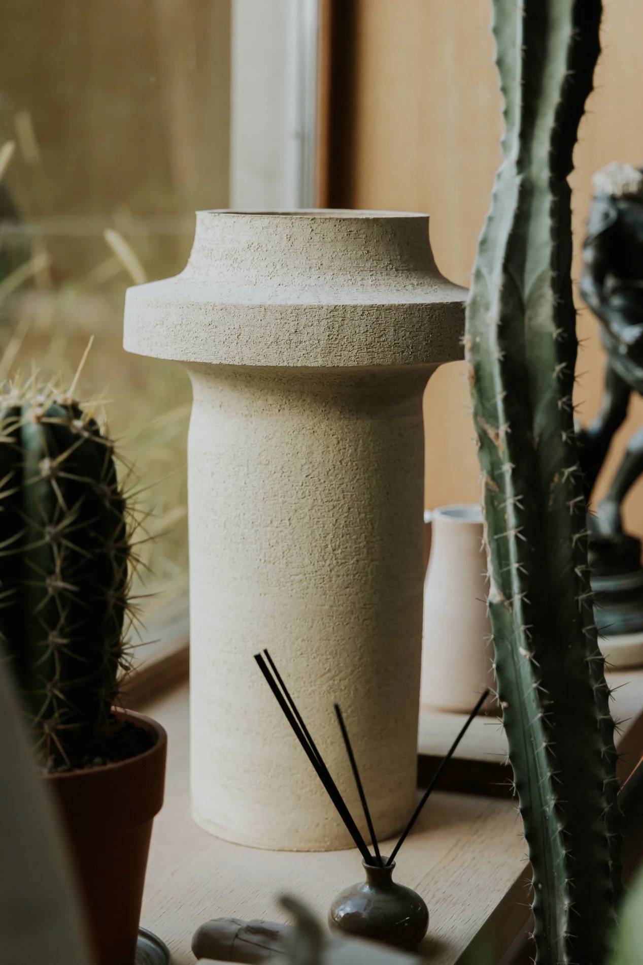 Lamp in maatwerk handgedraaid tussen cactussen en andere planten op een venstertablet.