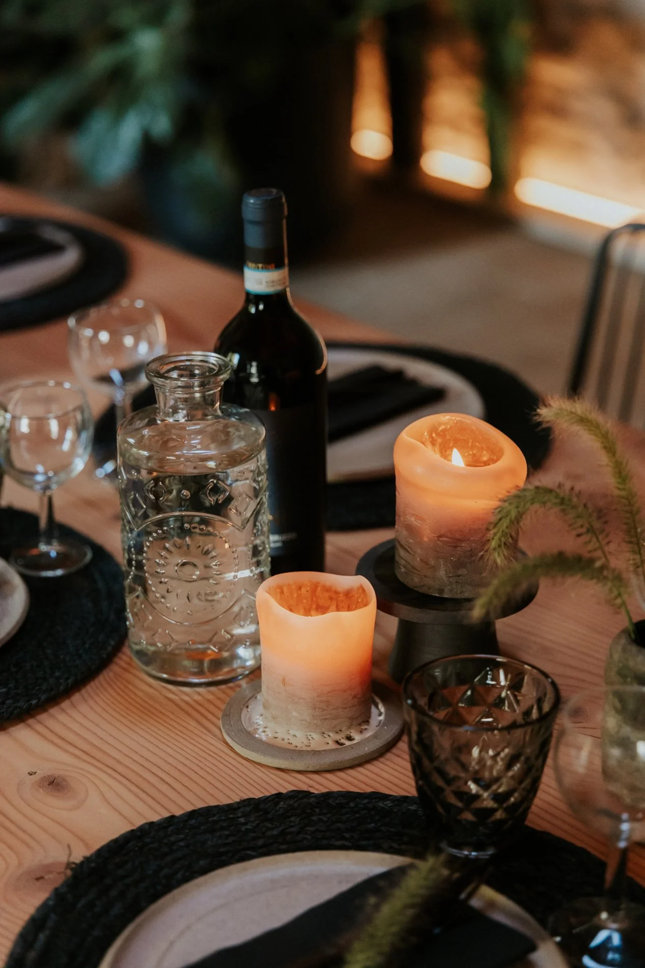 Een gedekte houten eettafel met kaarslicht, een fles wijn, wijnglazen, een waterkaraf en decoratieve elementen, in een gezellige, intieme sfeer.