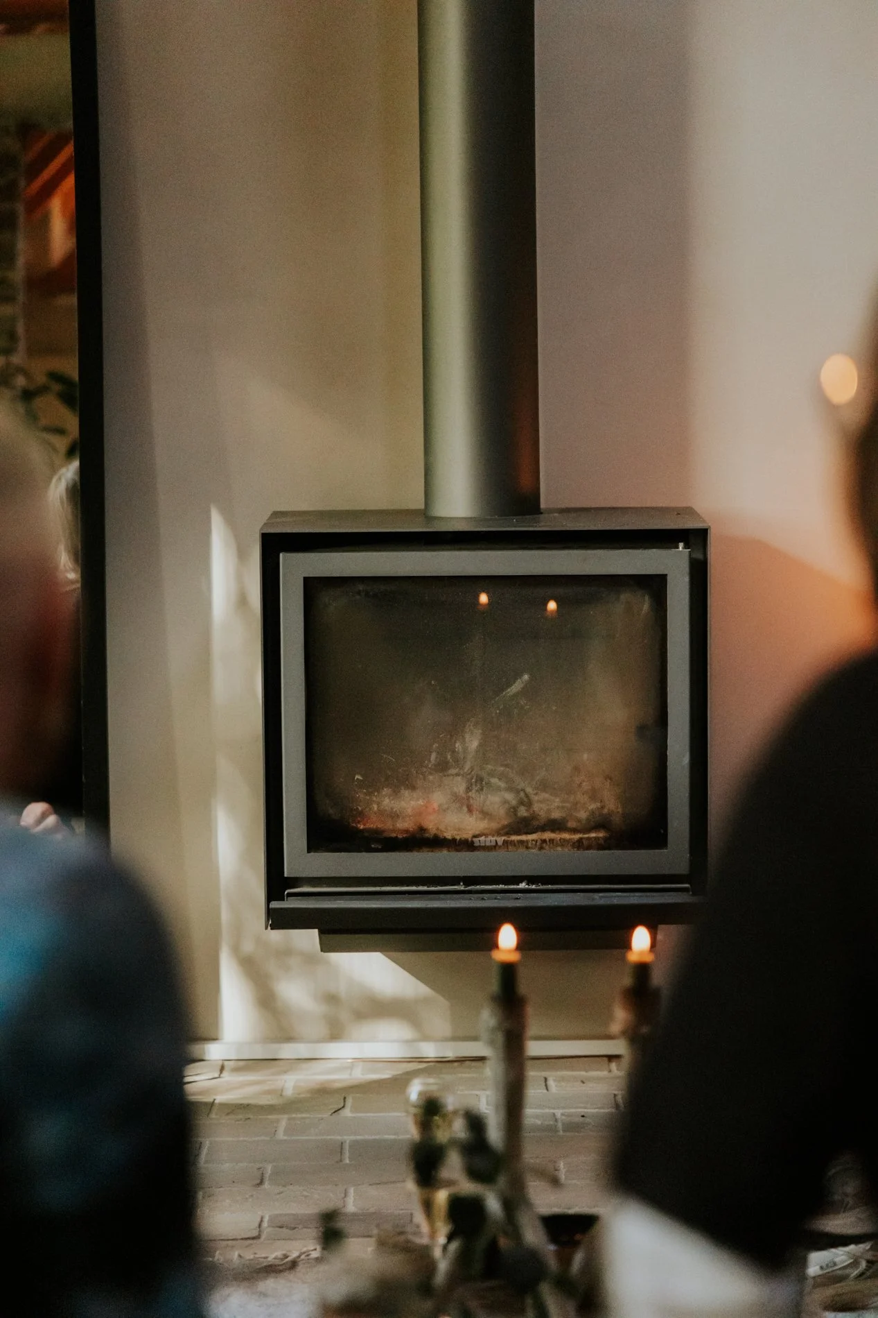 Binnenbeeld van een haard met een metalen afvoerbuis, kinderen die voor de haard zitten en kaarsen.