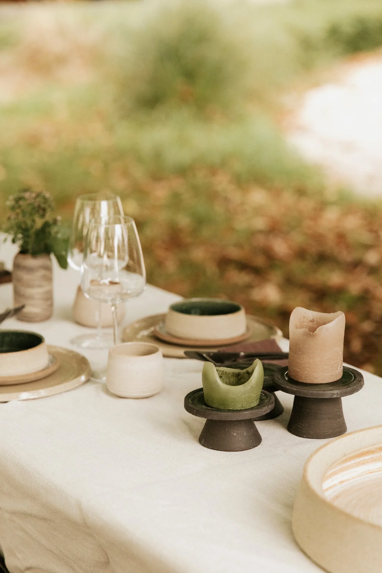 Een tafel met diverse keramische kommen en kandelaars, enkele glazen en planten op een witte tafel, met een achtergrond van herfstbladeren.