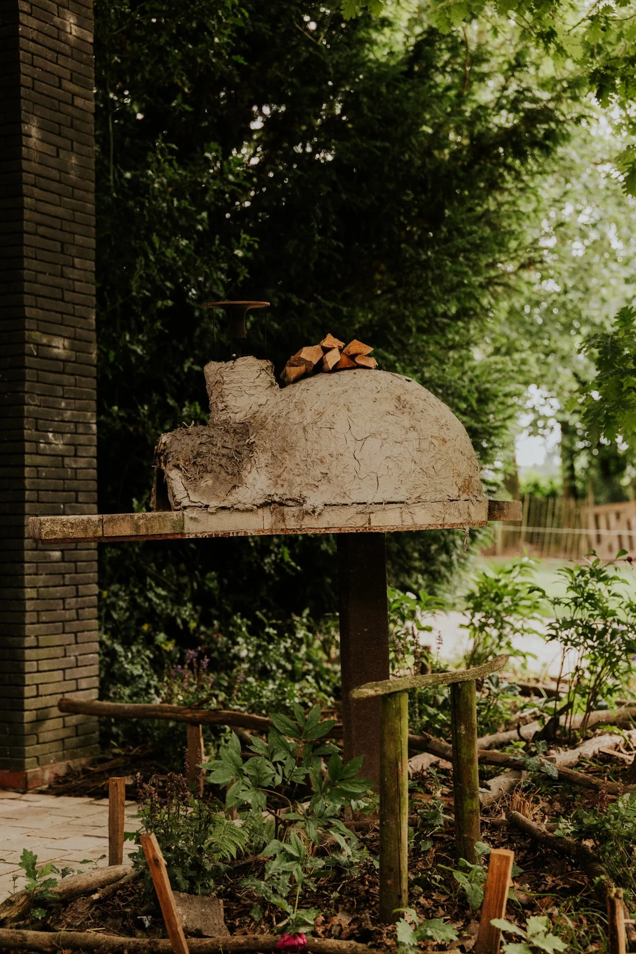 Pizza houtoven de achterzijde met daarop houtblokken en aanzicht tuin en terras.