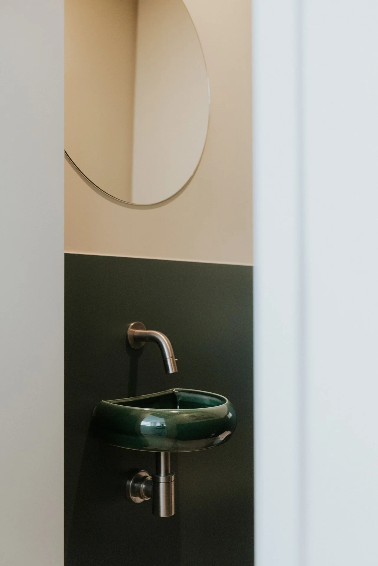 Detail handwasbakje in een toilet van een kantoor met een kraan en een spiegel, kleur groen en mortex.