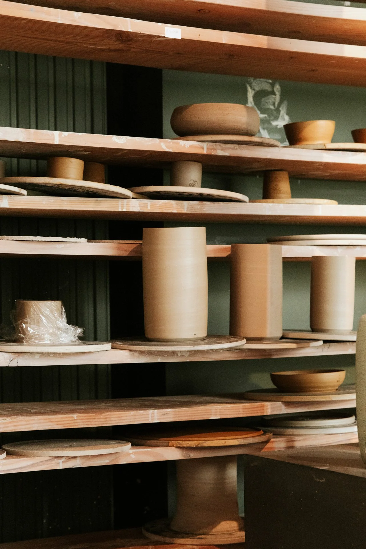 Rijen met ruw bewerkte keramische kommen en schalen op houten stellages in een pottenbakkerij.