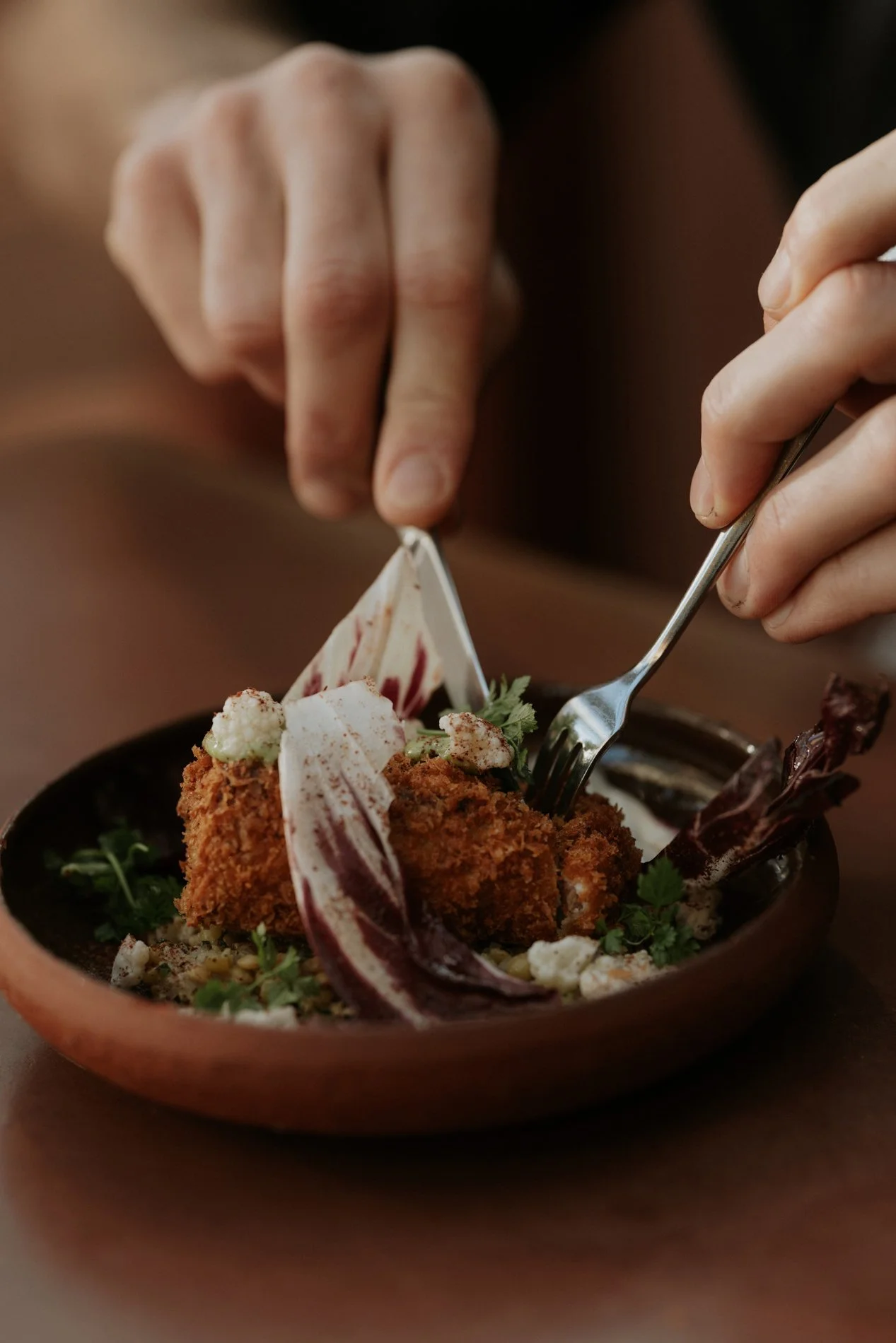 Rode kom met eten in op restaurant die aangesneden wordt, twee handen zichtbaar.  Atelier Pyotr Morf.