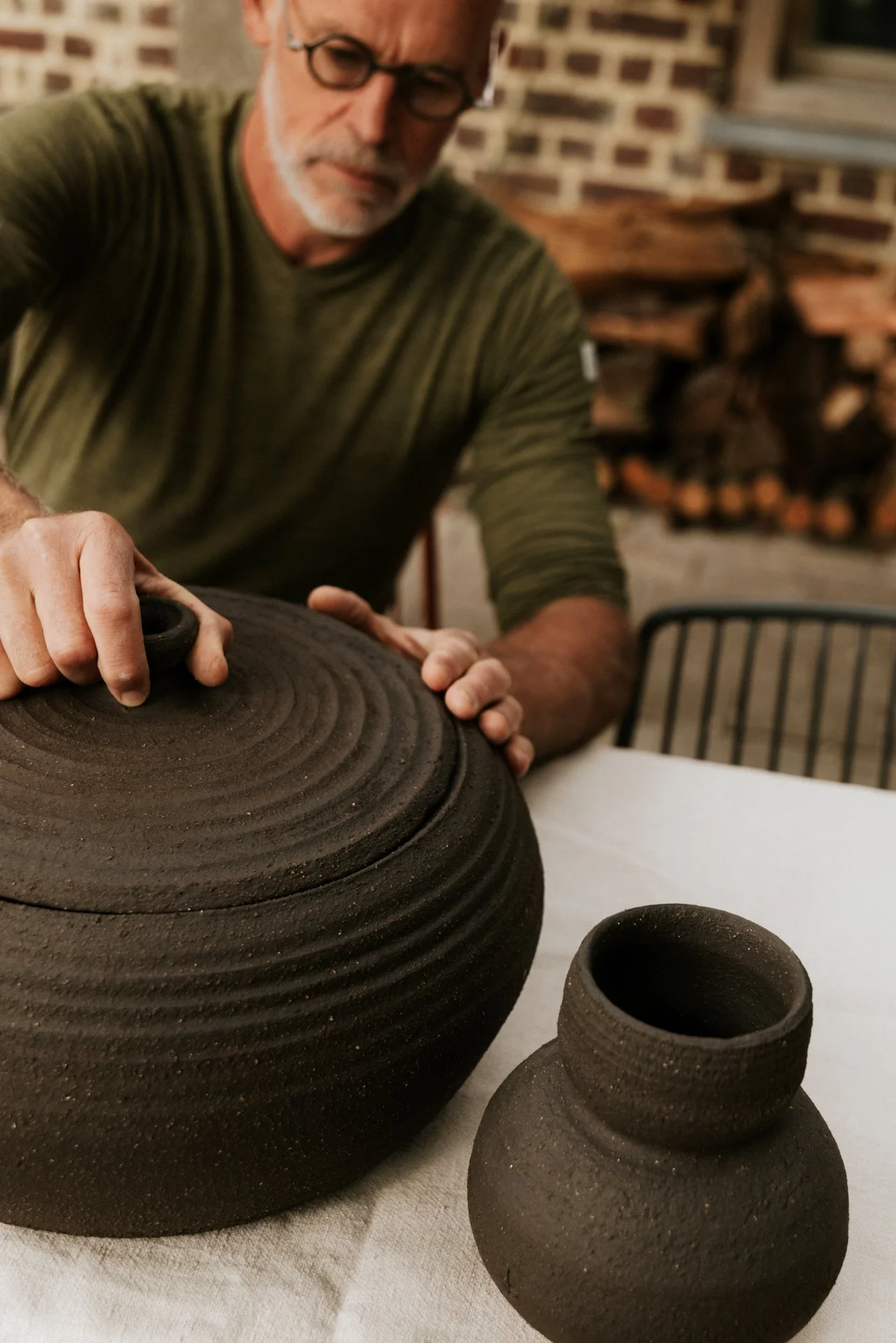 Keramist die zijn pot inspecteerd, zwarte pot en vaas op de voorgrond. Atelier Pyotr Morf