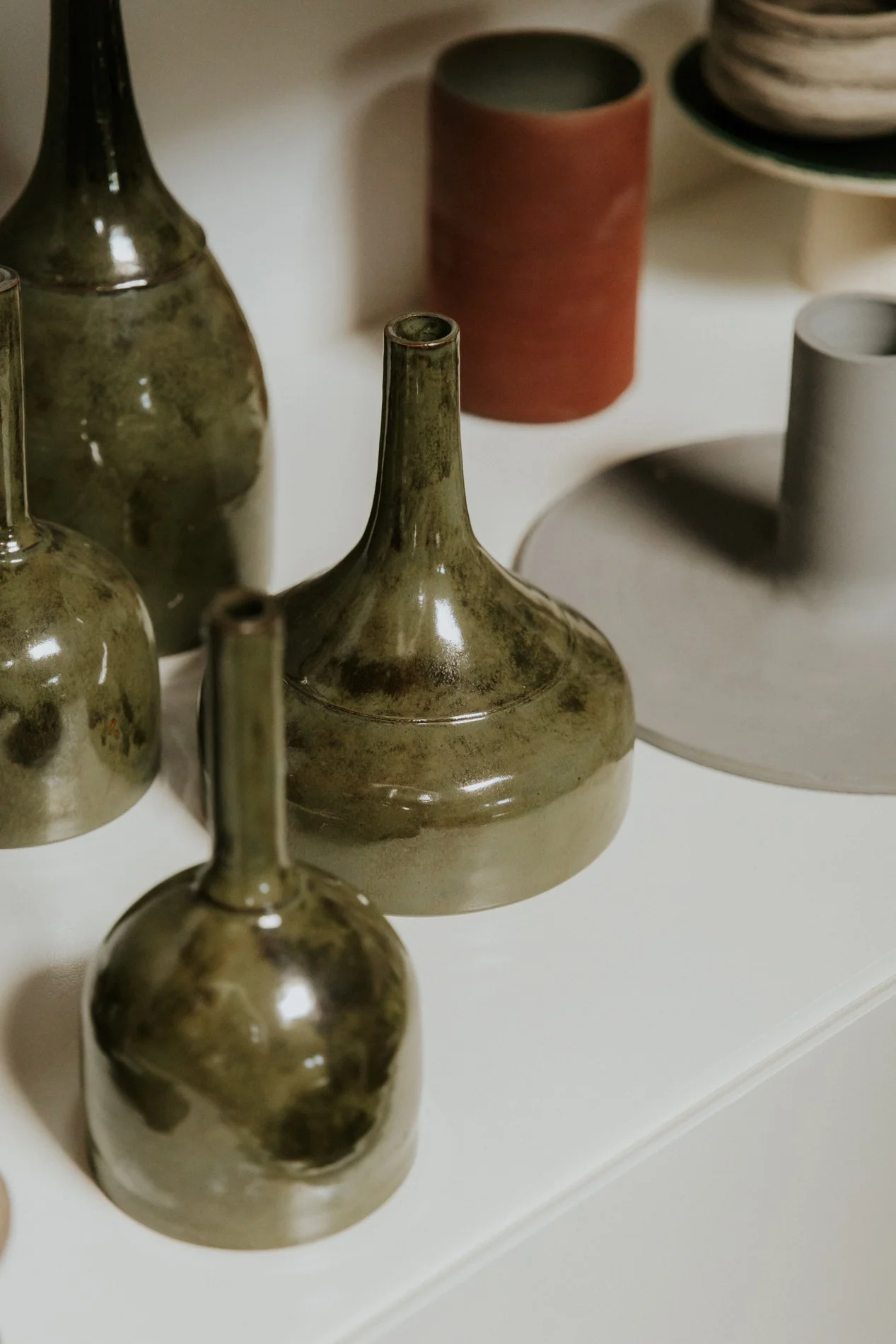 Groene keramiek hanglampen gepresenteerd op een wit meubel in een atelier.