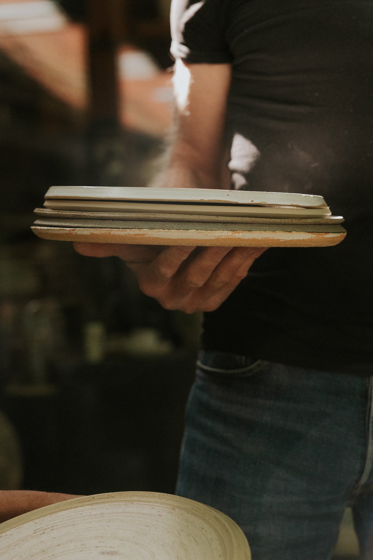 Stapel borden in de hand van een man met een zwart tshirt en een jeansbroek aan.  Atelier Pyotr Morf.