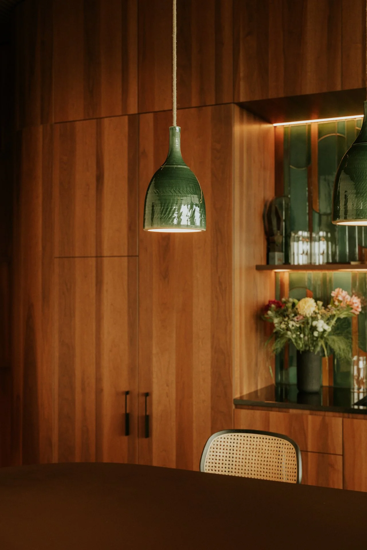 Hanglamp in keramiek in het groen in een eetplaats met op de achtergrond een kastenwand in hout.