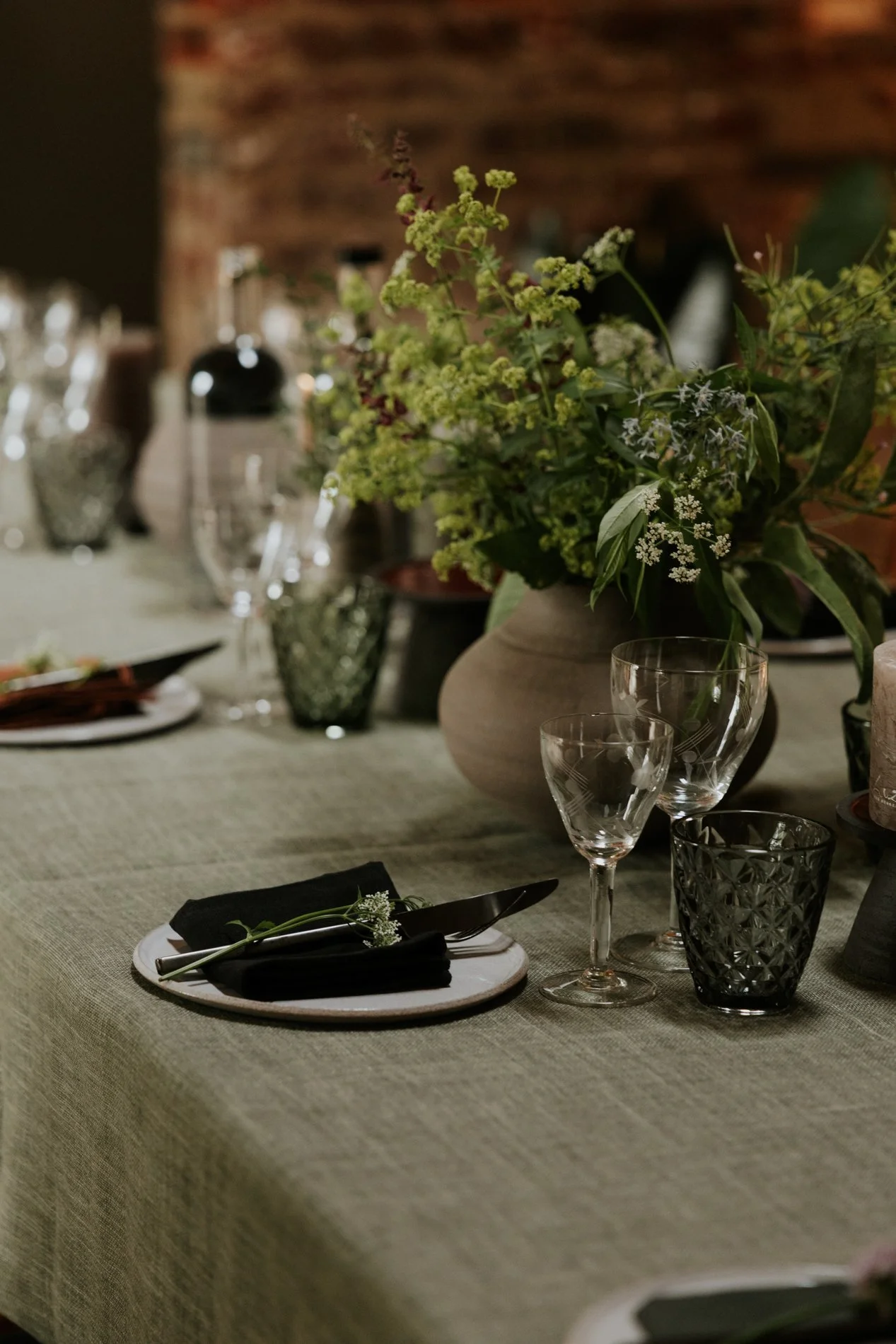 Een feesttafel met een bloemenarrangement, glazen en bestek onder een beige tafelkleed.