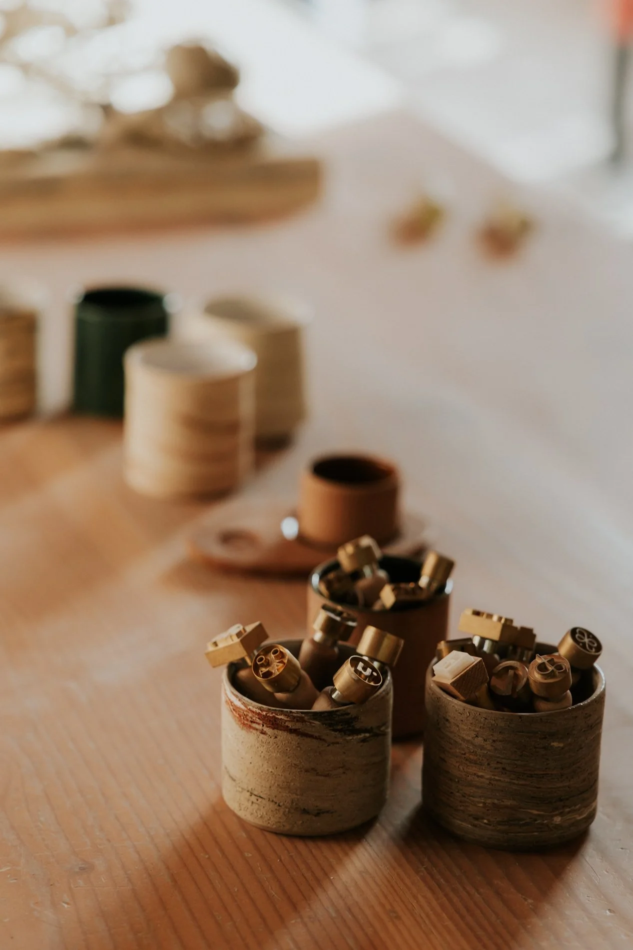 Stempels op de voorgrond op een tafel, achtergrond kopjes in keramiek in diverse kleuren.  Atelier Pyotr Morf.