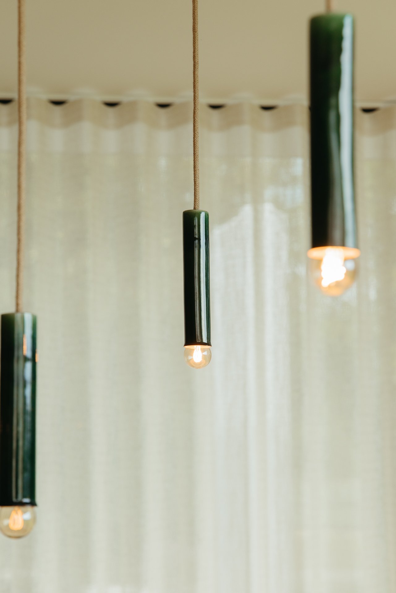 Hanglampen in keramiek aan een plafond met een wit doorzichtig gordijn op de achtergrond. 
