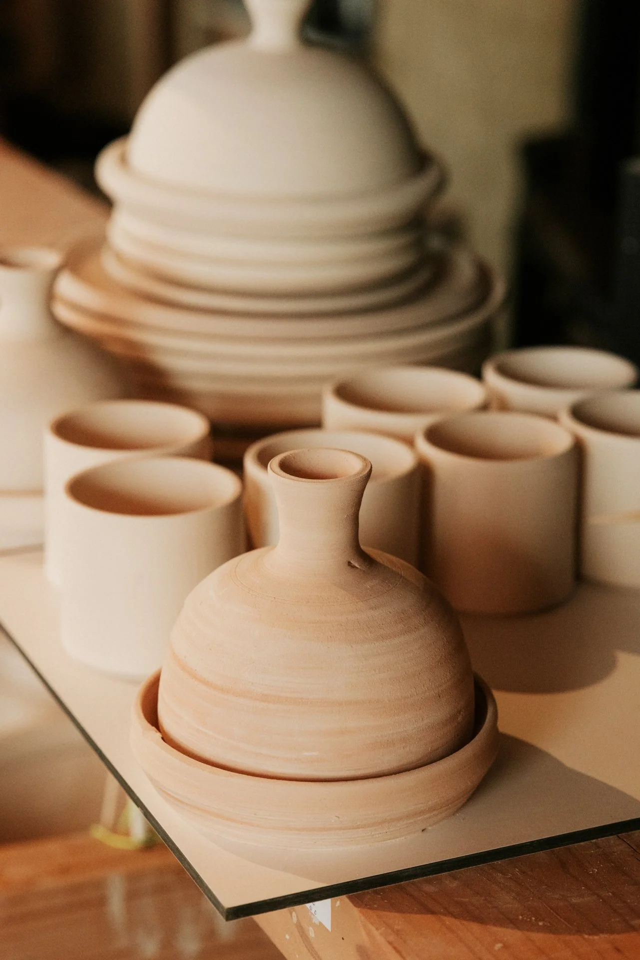 Tajine en andere keramiek klaar om geglazuurd te worden op een witte plank.  Atelier Pyotr Morf.