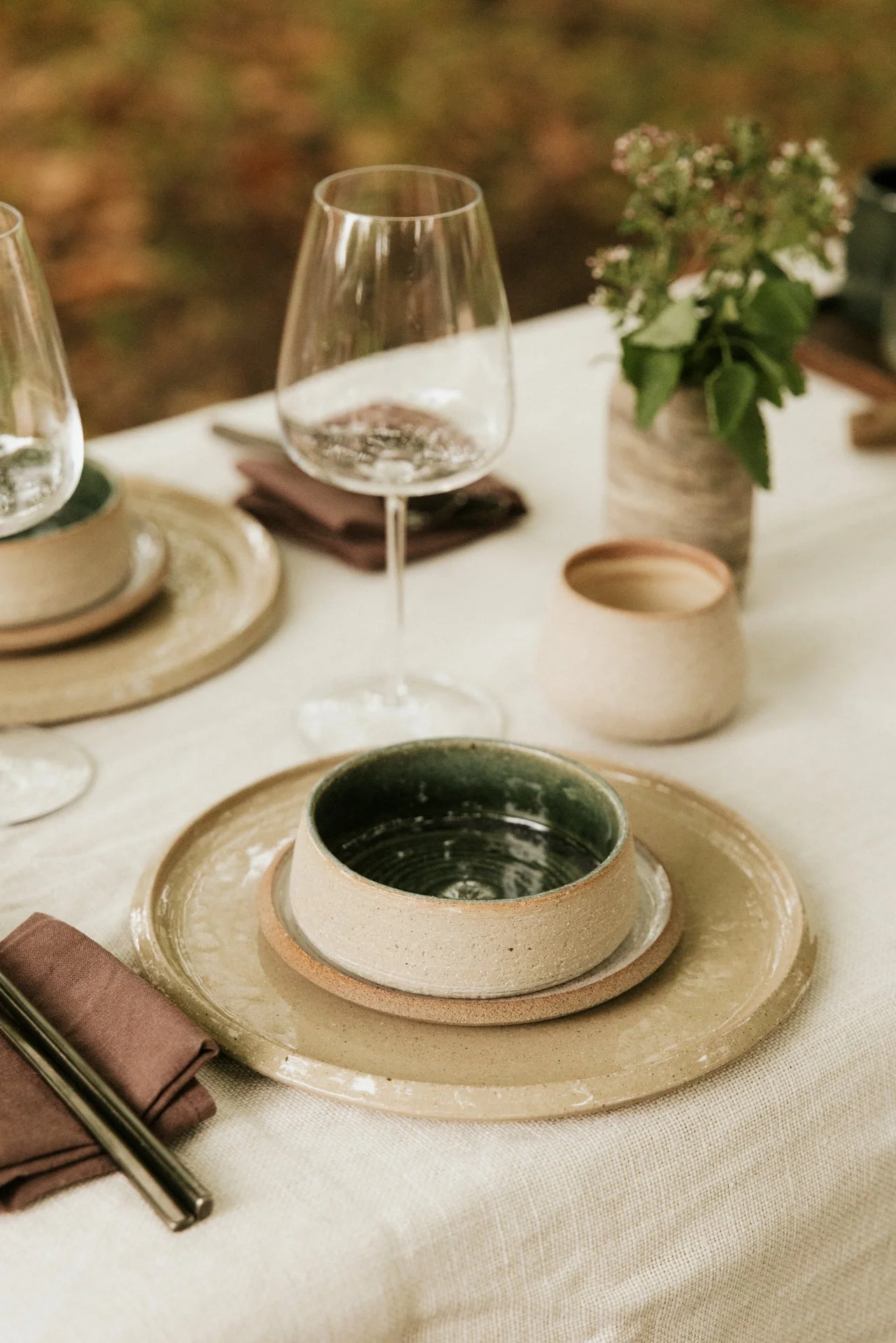 Gedenkte tafel met keramiek er op, kommen en borden, met een glas. Achtergrond tuin.  Atelier Pyotr Morf.