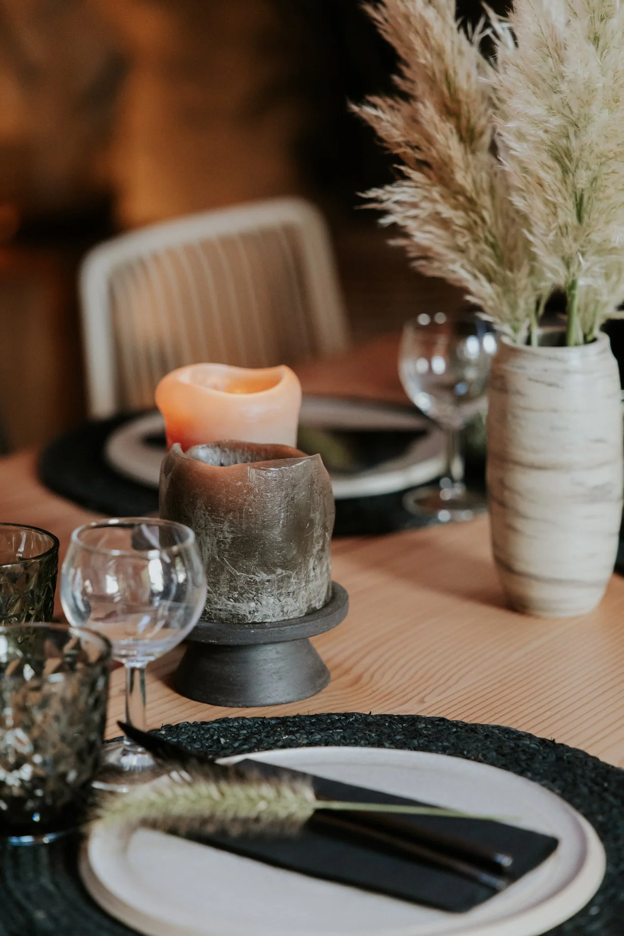 Een gedekte brunch tafel met kaarsen, een vaas met pampasgras, wijnglazen en servetten.