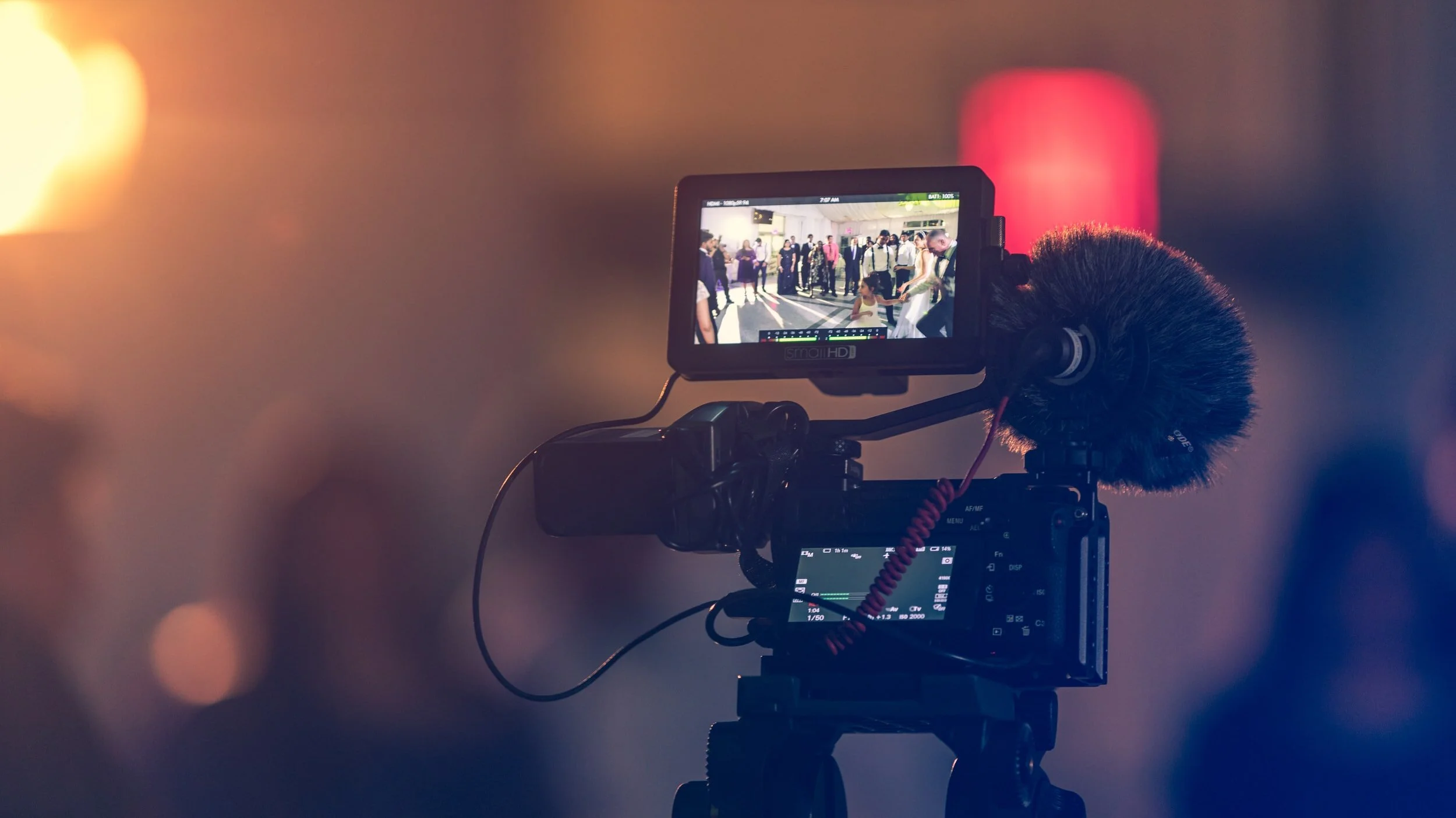 Camera with screen displaying a scene in progress, microphone attached, blurred background lighting.