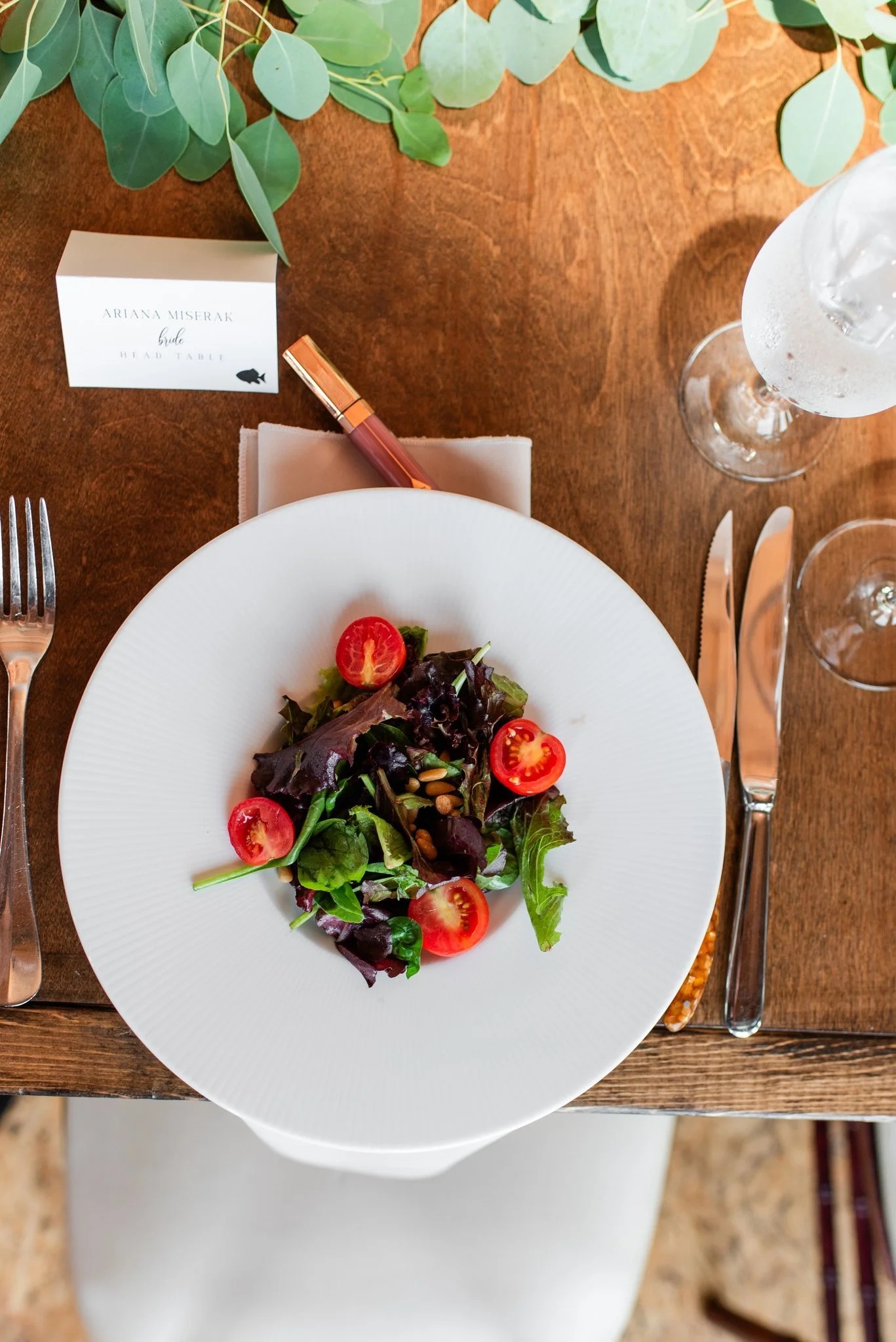 Salad with spring mix lettuce, cherry tomatoes, and pine nuts on a white plate and wood table.