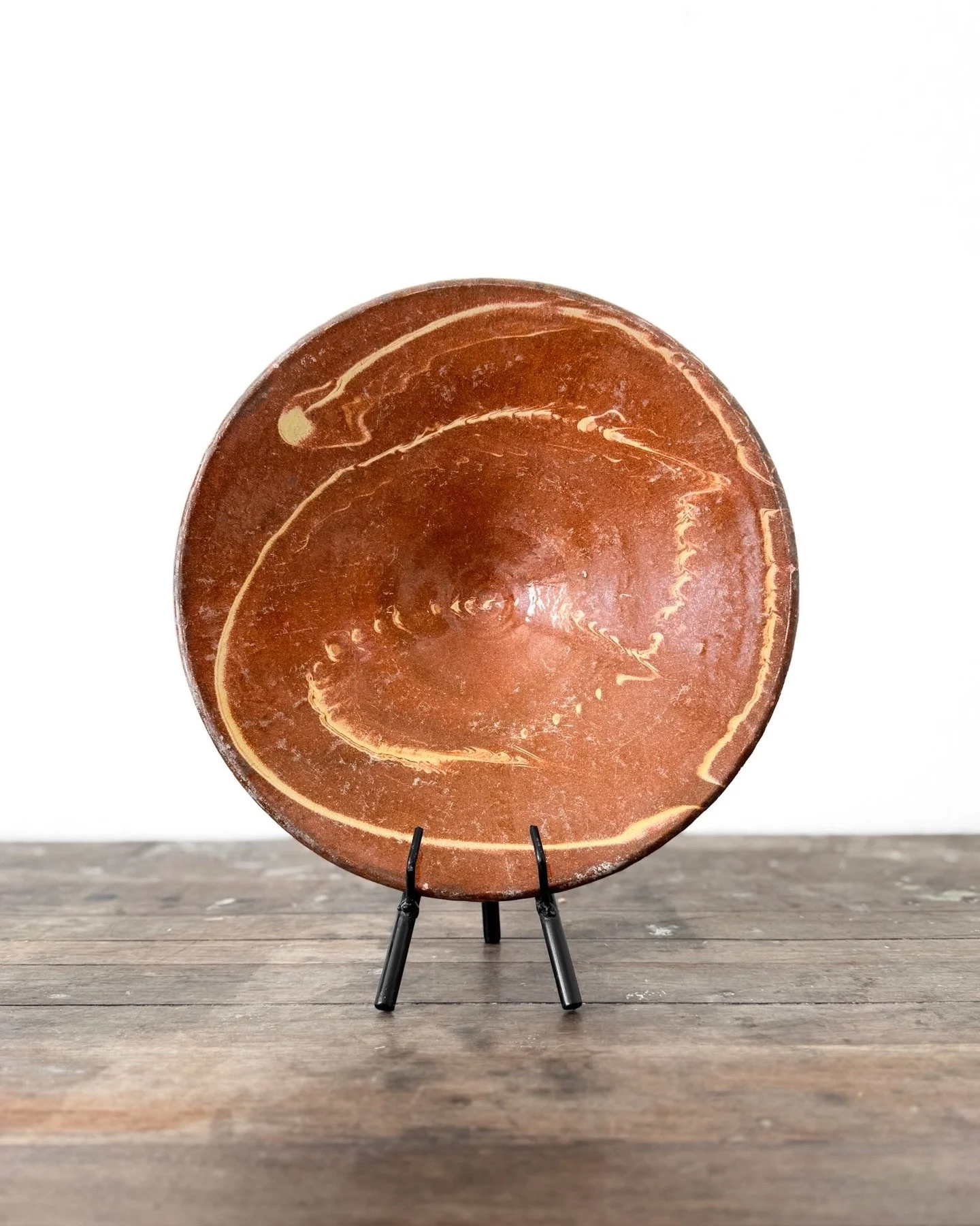 [Gift Idea!] An antique omelette-turning plate&mdash;hand-thrown, caramel-glazed, and slip-decorated&mdash;once helped home cooks flip the perfect omelette. Now, displayed on an iron easel, it brings rustic warmth and story-rich charm to a shelf in a