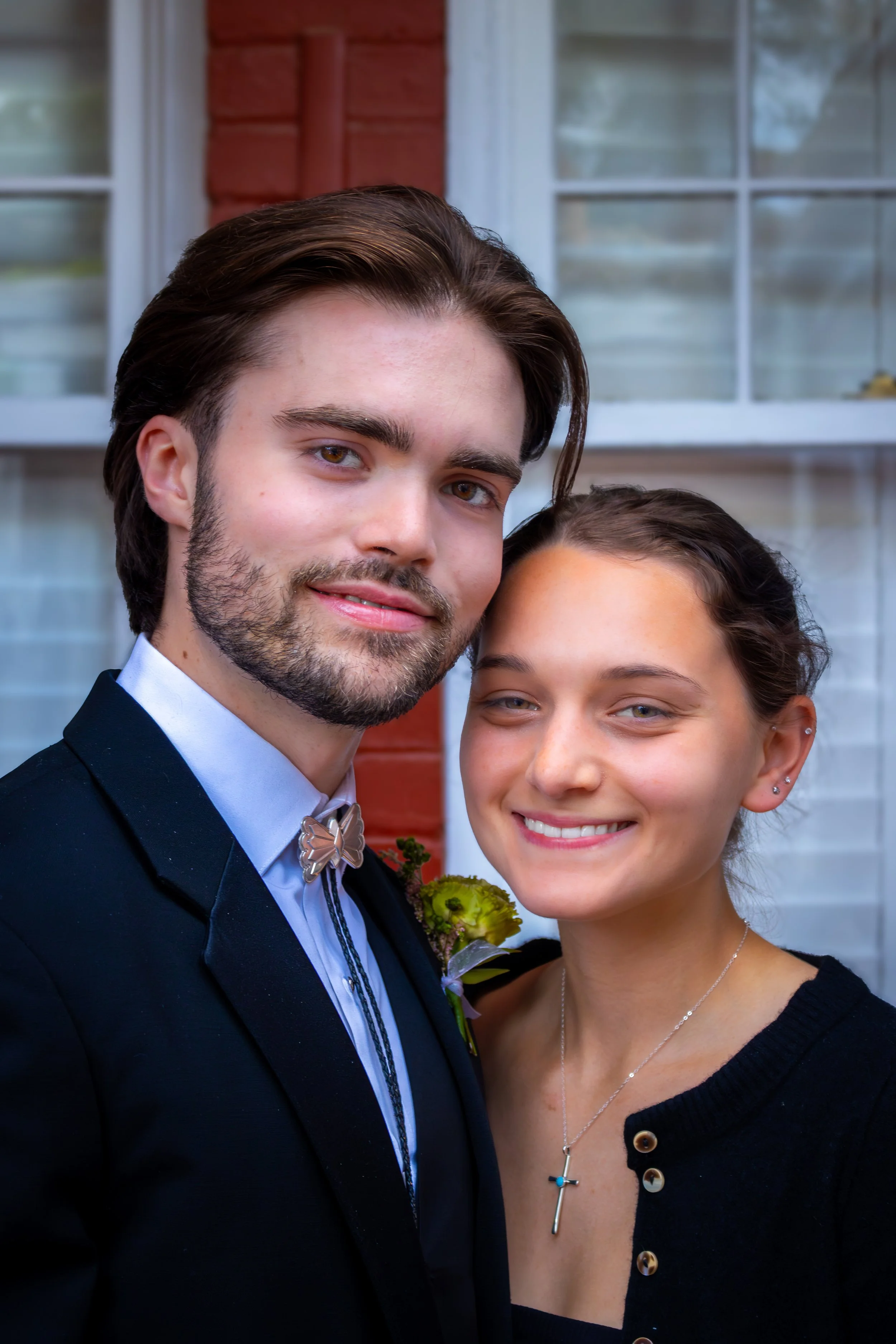 A young man and woman smiling close together in front of a house.
