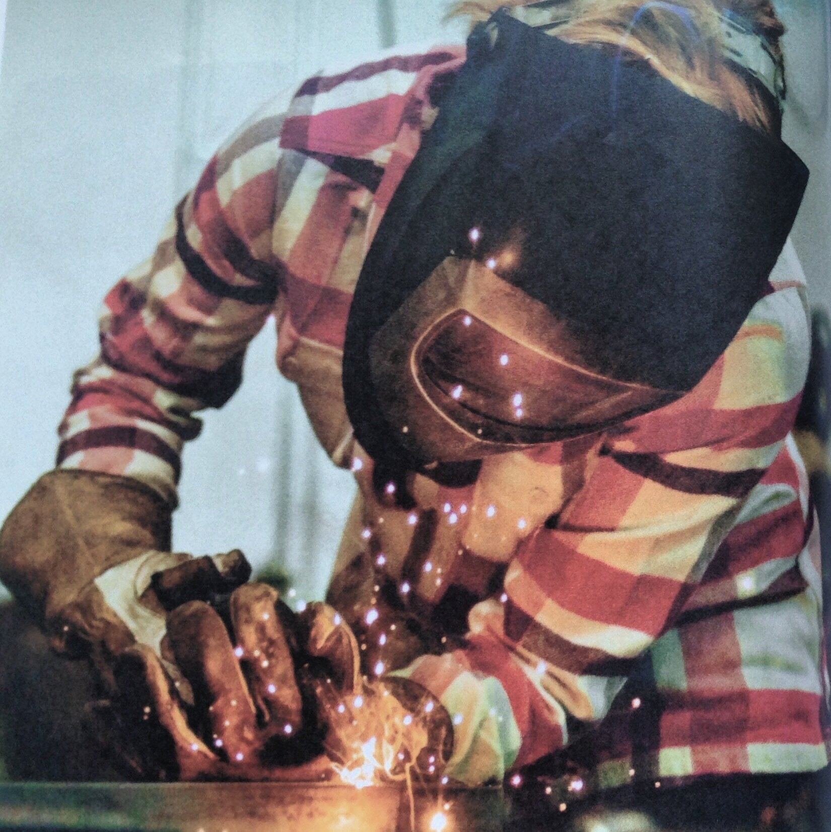 A person wearing a welding helmet and gloves is welding metal, with sparks flying around.