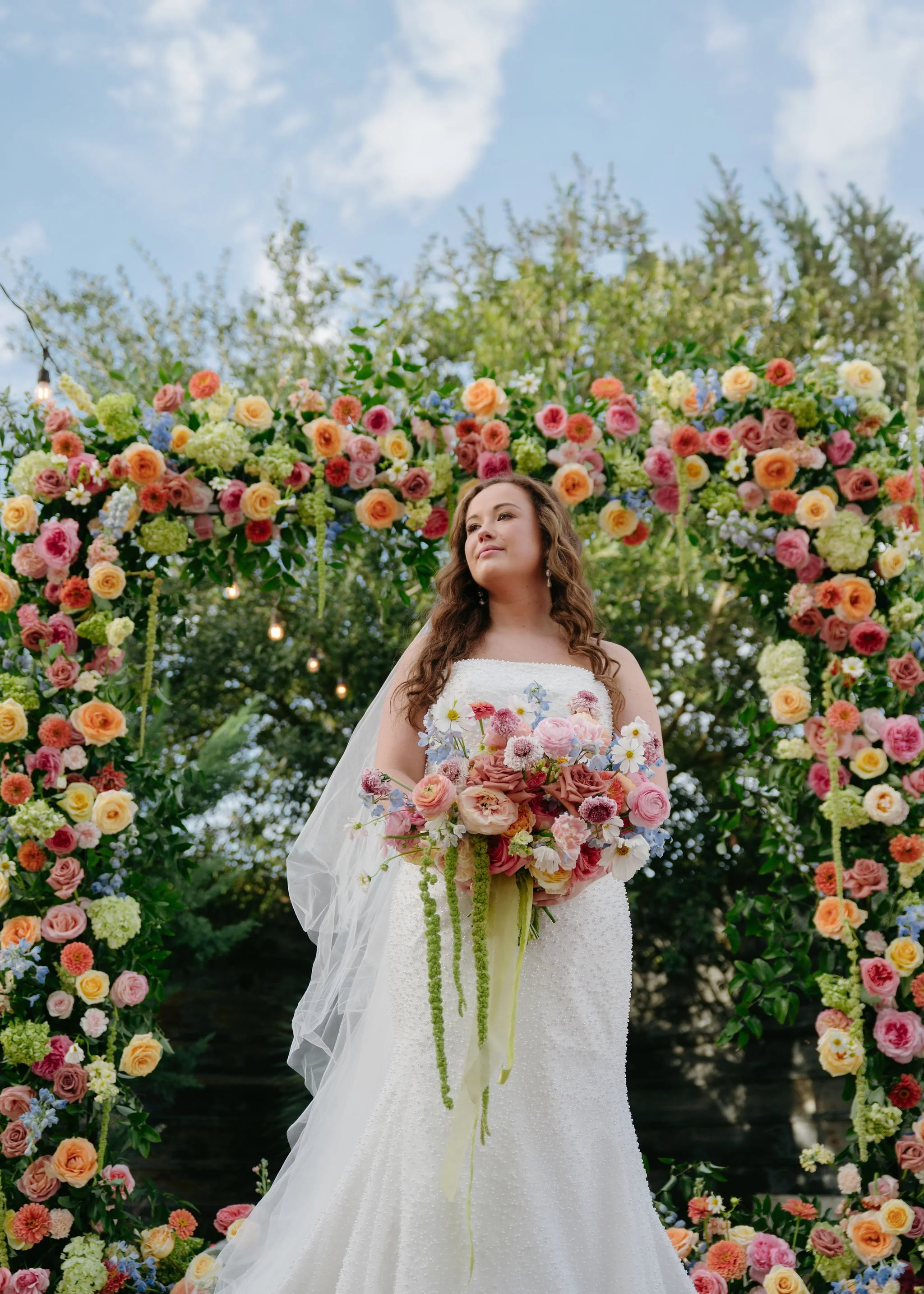 Bride holding a lush bouquet with a colorful floral arch behind her, designed and created by a top College Station florist.