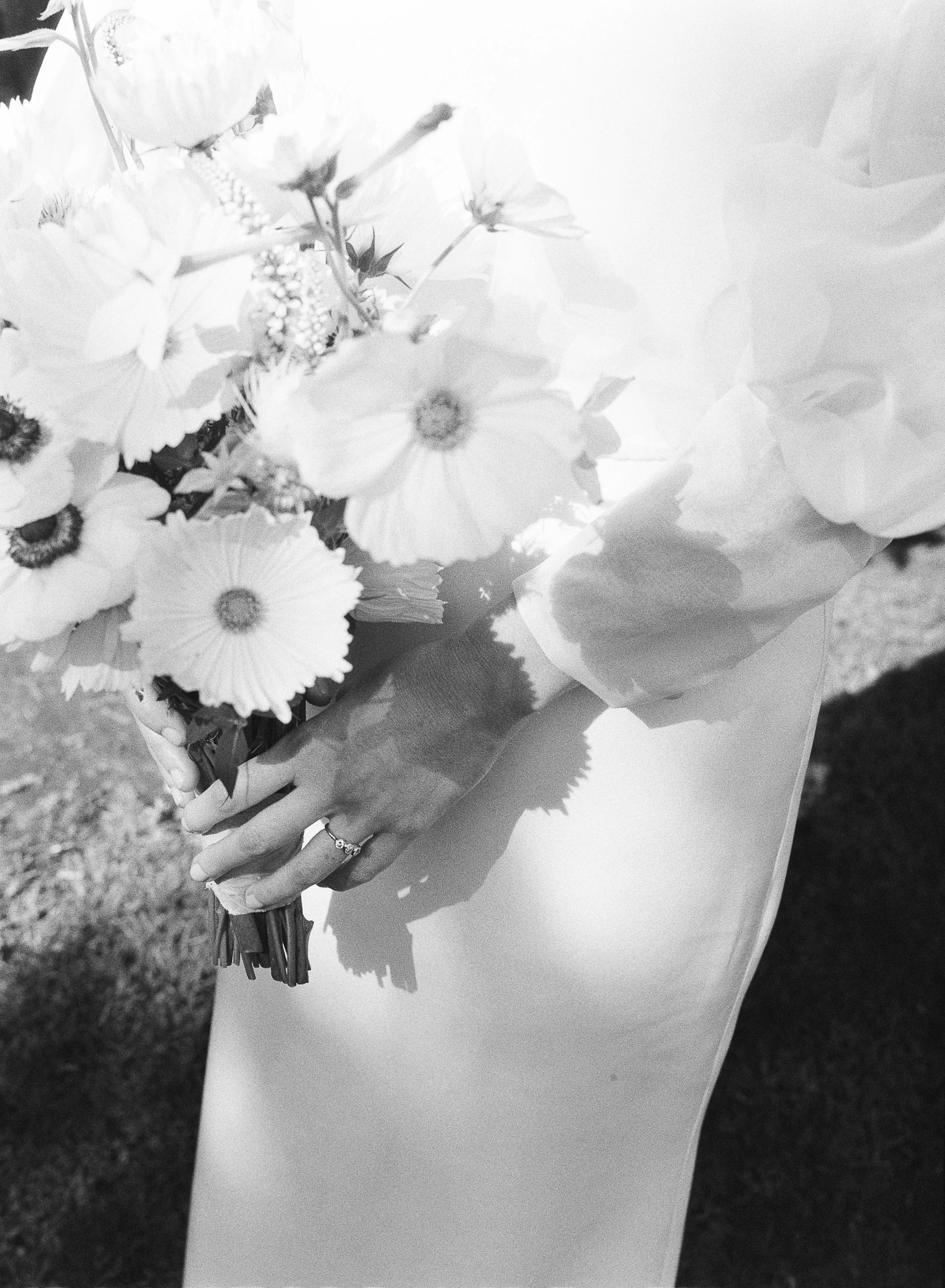 A person holding a bouquet of flowers while wearing a ring on their finger, with patterned shadows cast on a table surface.