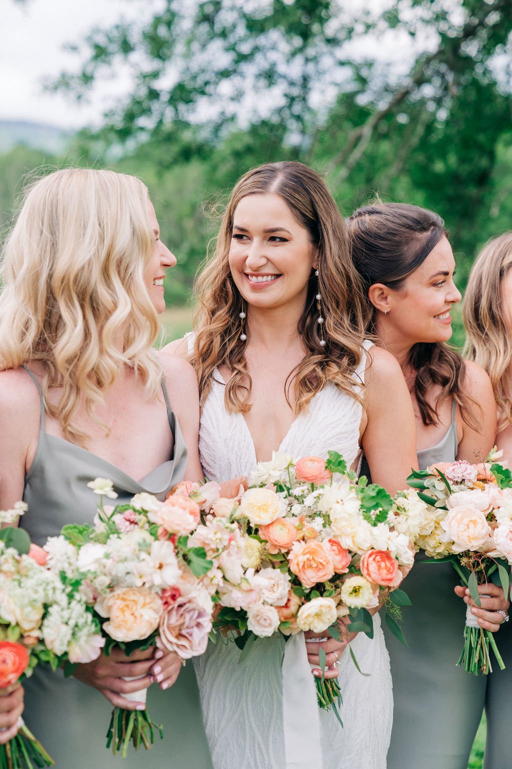 Women in pastel dresses holding bouquets at an outdoor gathering.