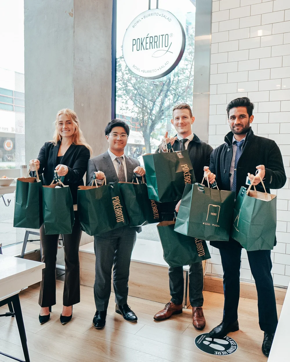 Four people holding Pokerrito takeaway bags inside a restaurant